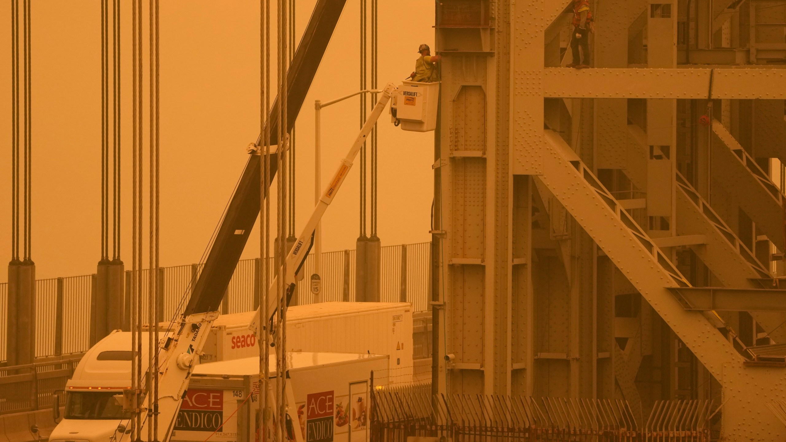 File - Workmen tend to the George Washington Bridge, as seen from Fort Lee, N.J., as haze from wildfires in Canada settles over the area on Wednesday, June 7, 2023. The haze from the wildfires is taking its toll on outdoor workers along the Eastern U.S. who carried on with their jobs even as dystopian orange skies forced the cancelation of sports events, school field trips and Broadway plays. (AP Photo/Seth Wenig, File)