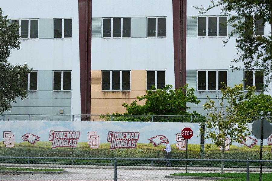 FILE - A security agent walks alongside a barrier surrounding Marjory Stoneman Douglas High School, July 5, 2023, in Parkland, Fla. Florida lawmakers and others on Saturday, Oct. 14, toured the school's 1200 Building, where a former student shot 17 people to death and wounded 17 others on Valentine's Day in 2018. The local school district has announced the 1200 Building will be demolished during the summer of 2024. (AP Photo/Rebecca Blackwell, File)