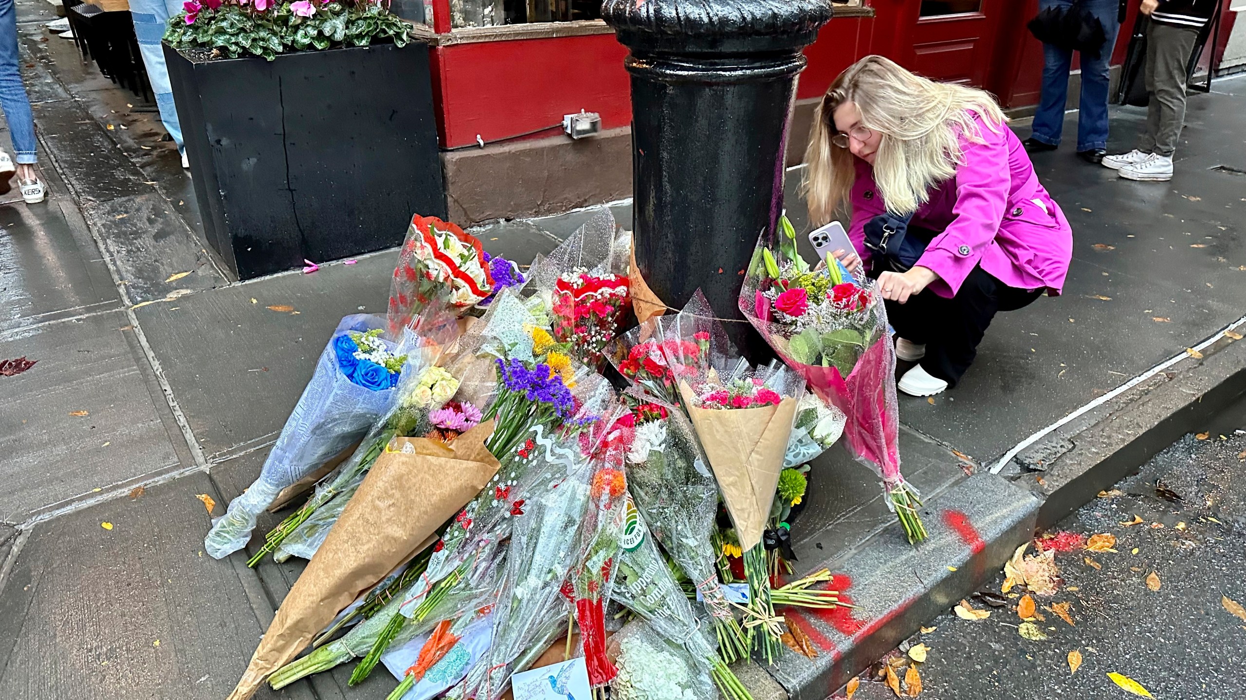 A person takes pictures of a makeshift memorial for Matthew Perry outside the building known as the "Friends" building in New York, Sunday, Oct. 29, 2023. Fans lingered in the rain, taking pictures and leaving flowers on the corner outside the building shown in exterior shots on the popular TV show. Perry, who played Chandler Bing on NBC’s “Friends” for 10 seasons, was found dead at his Los Angeles home on Saturday. He was 54. (AP Photo/Brooke Lansdale)