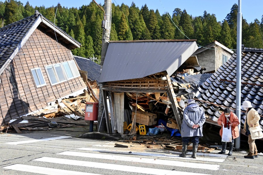 People look at collapsed buildings following earthquake in Wajima, Ishikawa prefecture, Japan Tuesday, Jan. 2, 2024. A series of powerful earthquakes in western Japan damaged homes, cars and boats, with officials warning people on Tuesday to stay away from their homes in some areas because of a continuing risk of major quakes and tsunamis. (Kyodo News via AP)