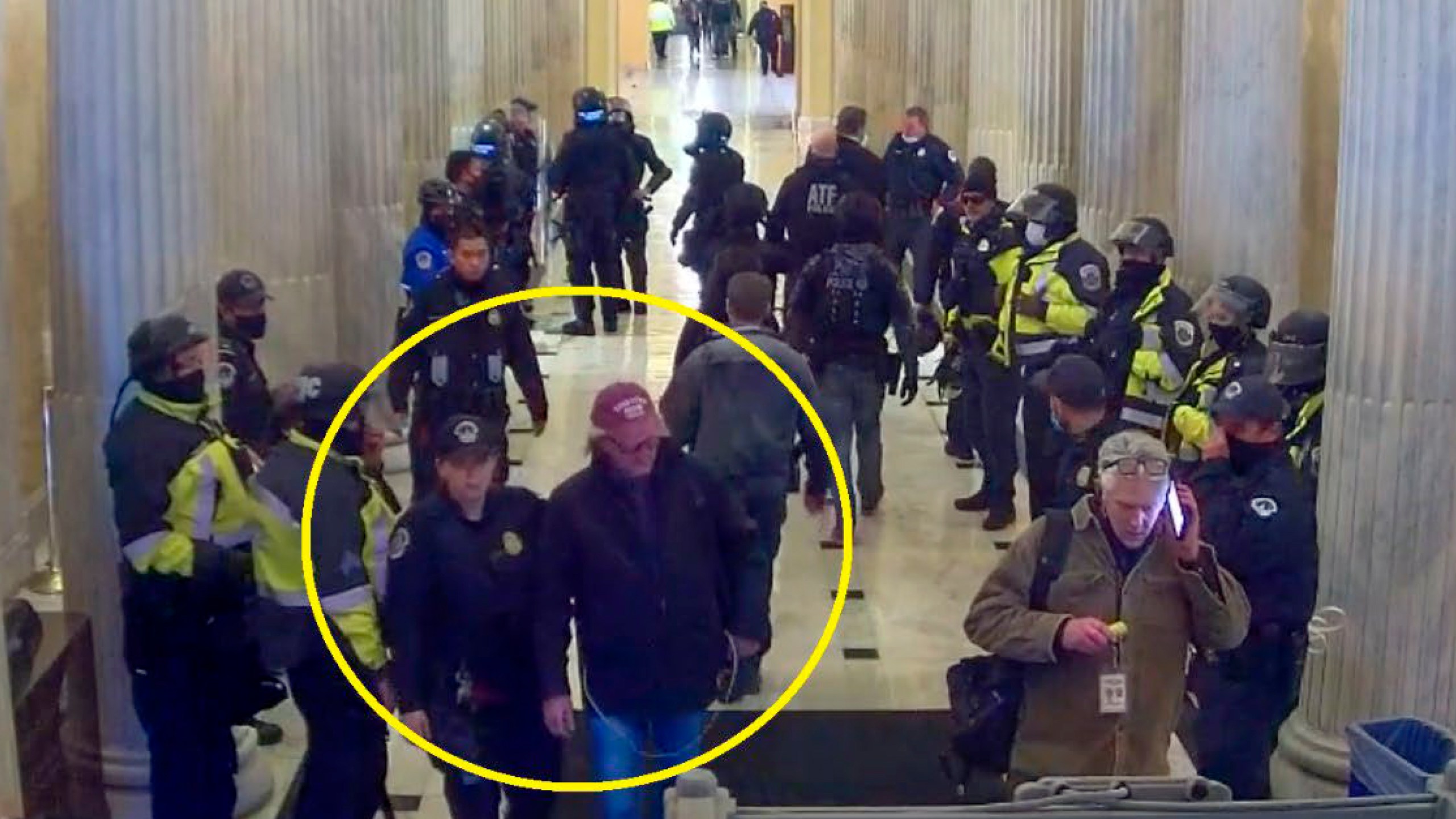 This image from U.S. Capitol Police video, contained and annotated in the Justice Department's statement of facts in support arrest warrant for Stephen Michael Baker, shows Baker, circled in yellow, being led from the U.S. Capitol on Jan. 6, 2021, in Washington, by a U.S. Capitol Police officer. Baker, a Texas-based writer for a conservative media outlet has surrendered to authorities to face charges that he joined a mob's attack on the U.S. Capitol on Jan. 6, 2021. (Department of Justice via AP)