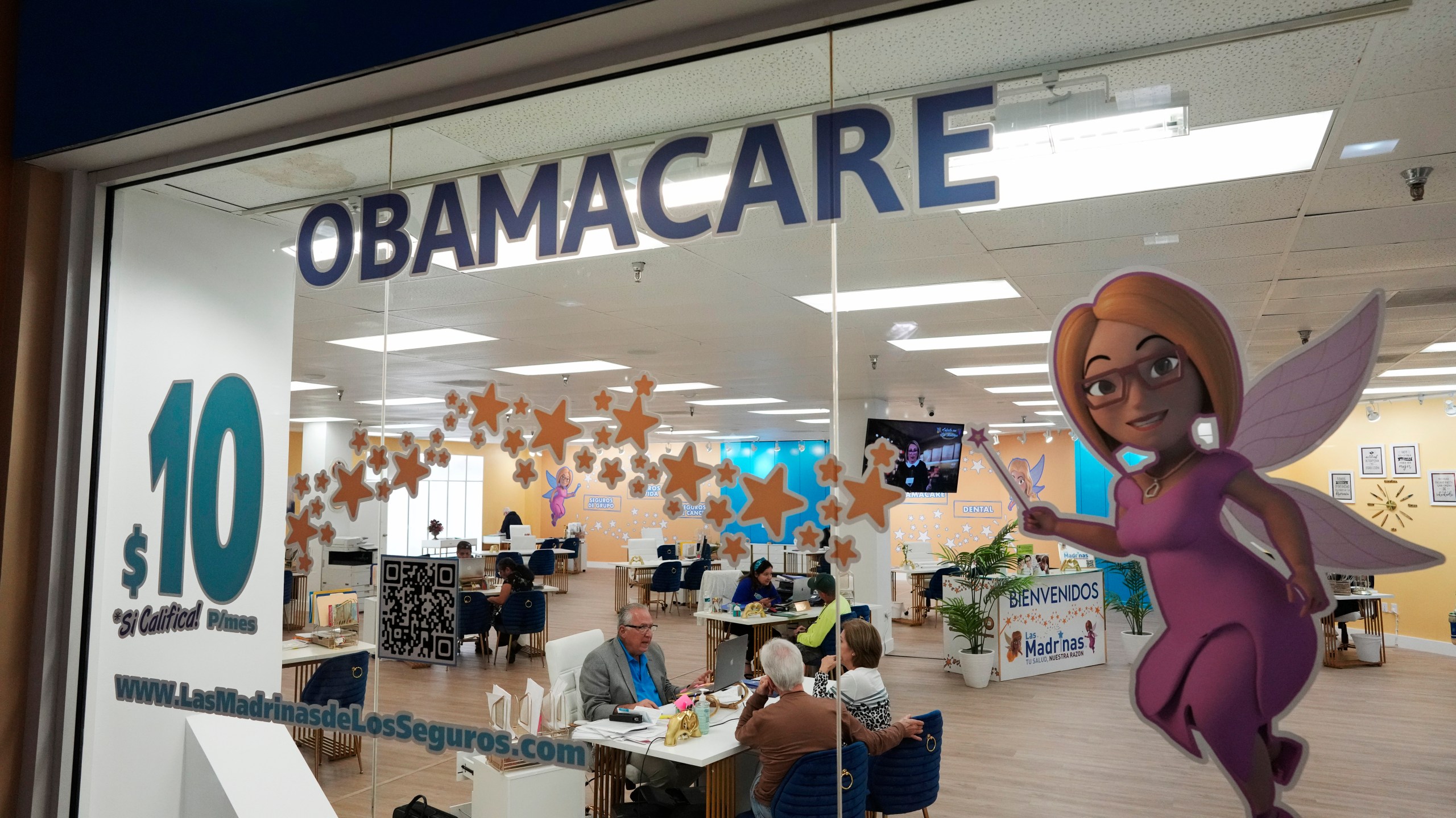 FILE - An insurance agent talks with clients inside the main location of Las Madrinas de los Seguros, Spanish for "The Godmothers of Insurance," at a shopping center in Miami, on Dec. 5, 2023. Roughly 100,000 immigrants who were brought to the U.S. are expected to enroll in the Affordable Care Act's health insurance next year under a new directive the Biden administration released Friday, May 3, 2024. (AP Photo/Rebecca Blackwell, File)