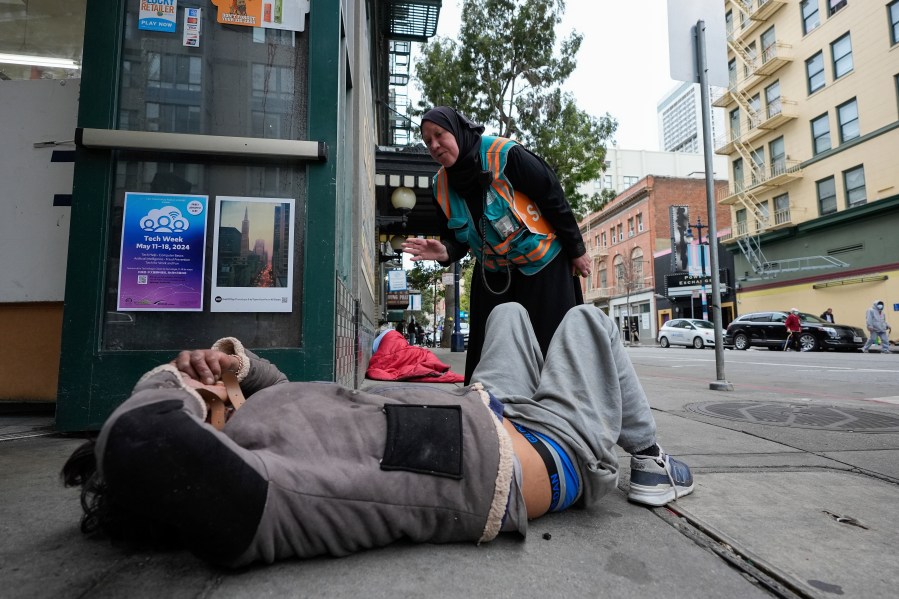 Tatiana Alabsi, right, checks on a man laying on a sidewalk and asks him to please move before children start walking to school in the Tenderloin neighborhood Wednesday, April 24, 2024, in San Francisco. (AP Photo/Godofredo A. Vásquez)