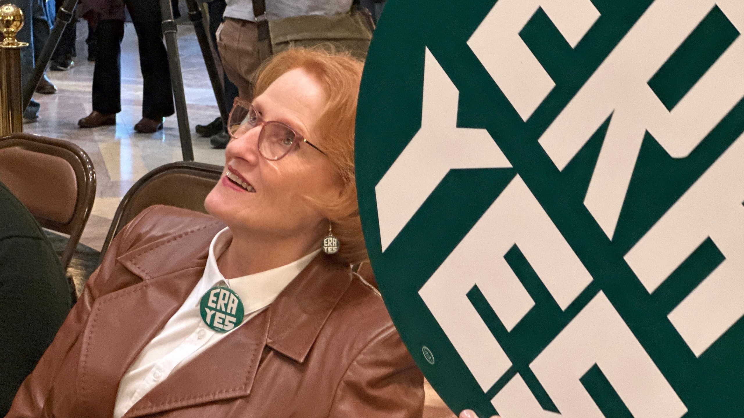 CORRECTS PHOTOGRAPHER TO STEVE KARNOWSKI - Betty Folliard, an advocate for the proposed Minnesota Equal Rights Amendment and the founder of ERA Minnesota, holds a green sign that says "ERA YES" during a rally in support of the proposal, March 7, 2024, in the Capitol building in St. Paul, Minn. The proposal would be among the most expansive protections of women's rights, abortion rights and LGBTQ rights in the nation if it is approved by lawmakers this session and then by Minnesota voters on the 2026 ballot. (AP Photo/Steve Karnowski)