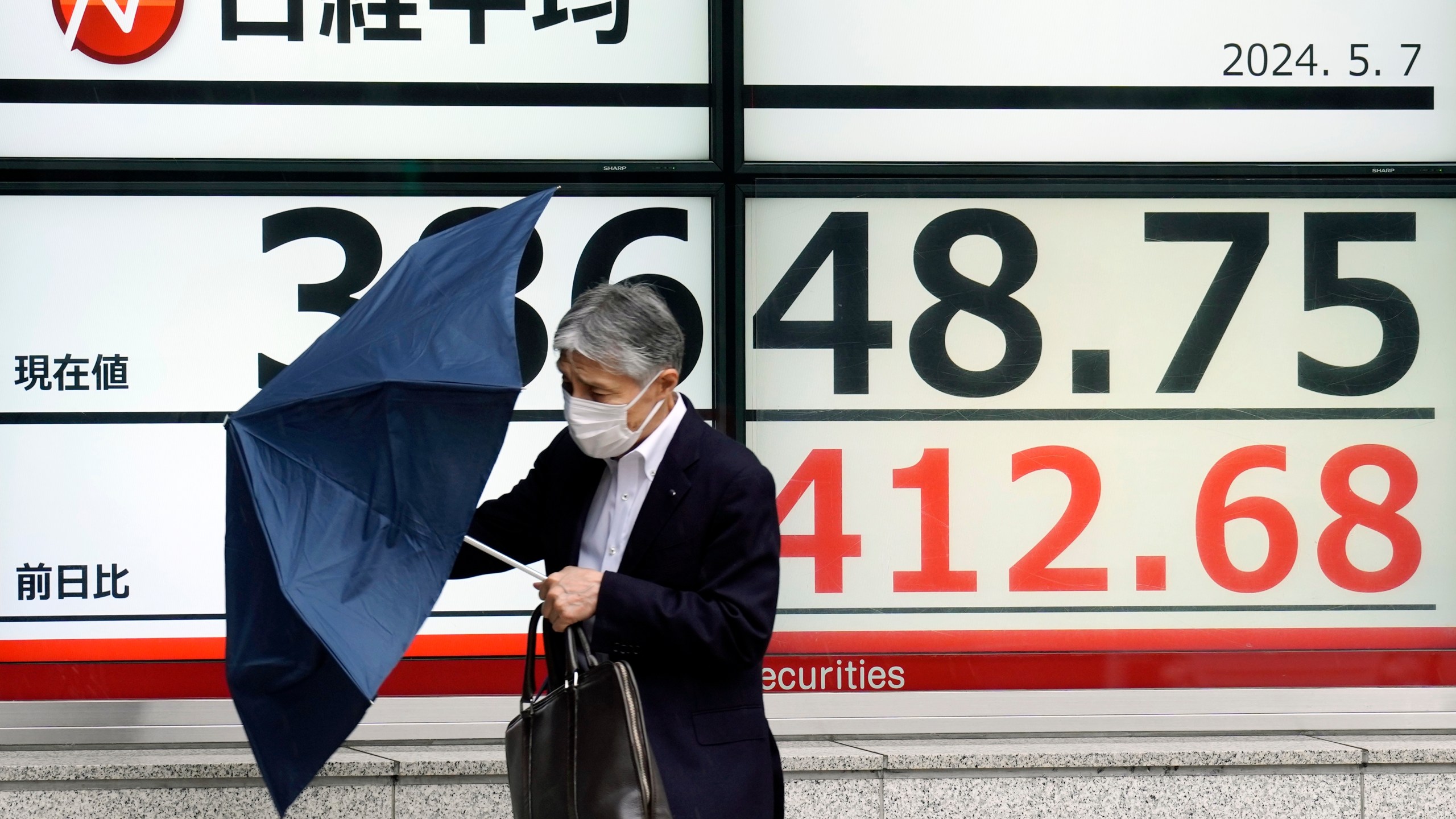 A person walks in the rain near an electronic stock board showing Japan's Nikkei 225 index at a securities firm Tuesday, May 7, 2024, in Tokyo. (AP Photo/Eugene Hoshiko)