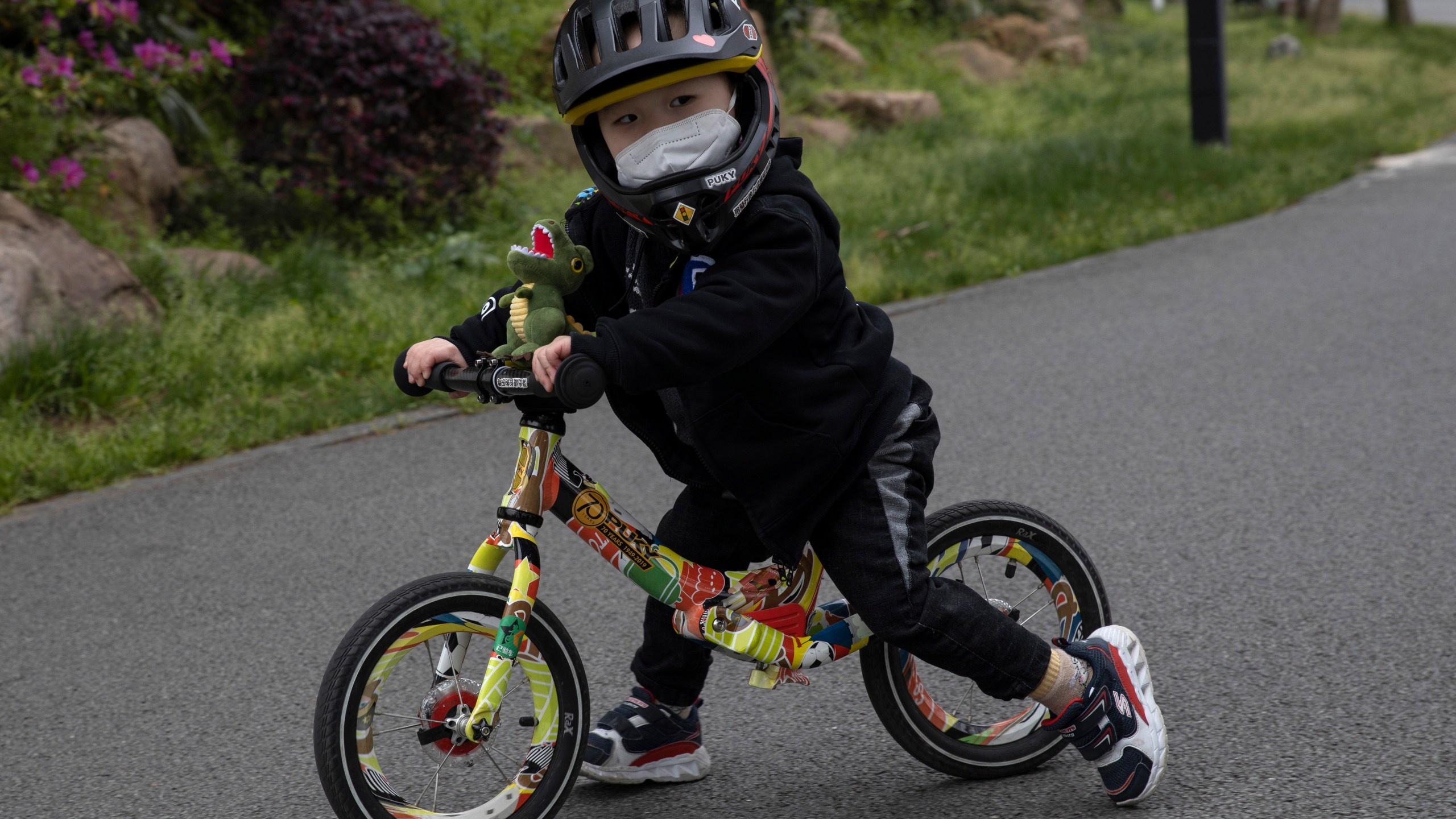 FILE - A child wearing a mask pushes his bike during a quiet day at the East Lake Park in Wuhan in central China's Hubei province, April 2, 2020. Miniature bikes with no pedals seem to be everywhere these days, and the kids riding them are getting younger and younger. Experts recommend starting with those so-called balance bikes at a younger-than-expected age, possibly even less than a year old. (AP Photo/Ng Han Guan, File)