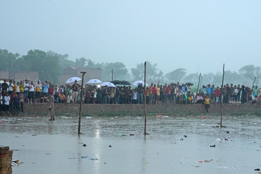 Villagers watch officials visit the site of Tuesday's stampede as it rains in Hathras district, Uttar Pradesh, India, Wednesday, July 3, 2024. Severe overcrowding and a lack of exits contributed to a stampede at a religious festival in northern India, authorities said Wednesday, leaving more than 100 people dead as the faithful surged toward the preacher to touch him and chaos ensued. (AP Photo/Rajesh Kumar Singh)