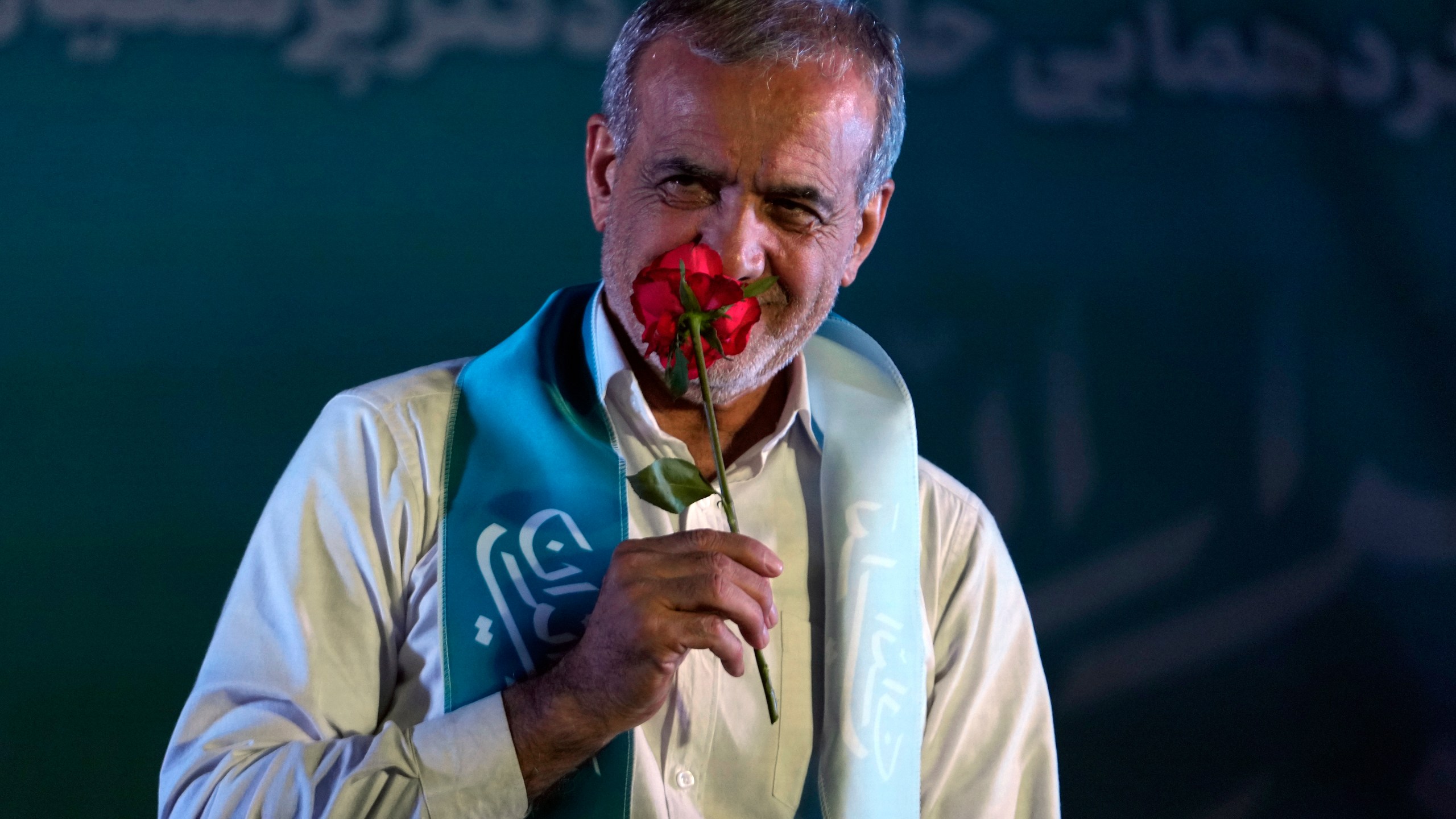 Reformist candidate for the Iran's presidential election Masoud Pezeshkian smells a flower during a campaign rally in Tehran, Iran, Wednesday, July 3, 2024. Comments suggesting that Iran's reformist presidential candidate could increase government-set gasoline prices have raised fears of a repeat of nationwide protests. (AP Photo/Vahid Salemi)