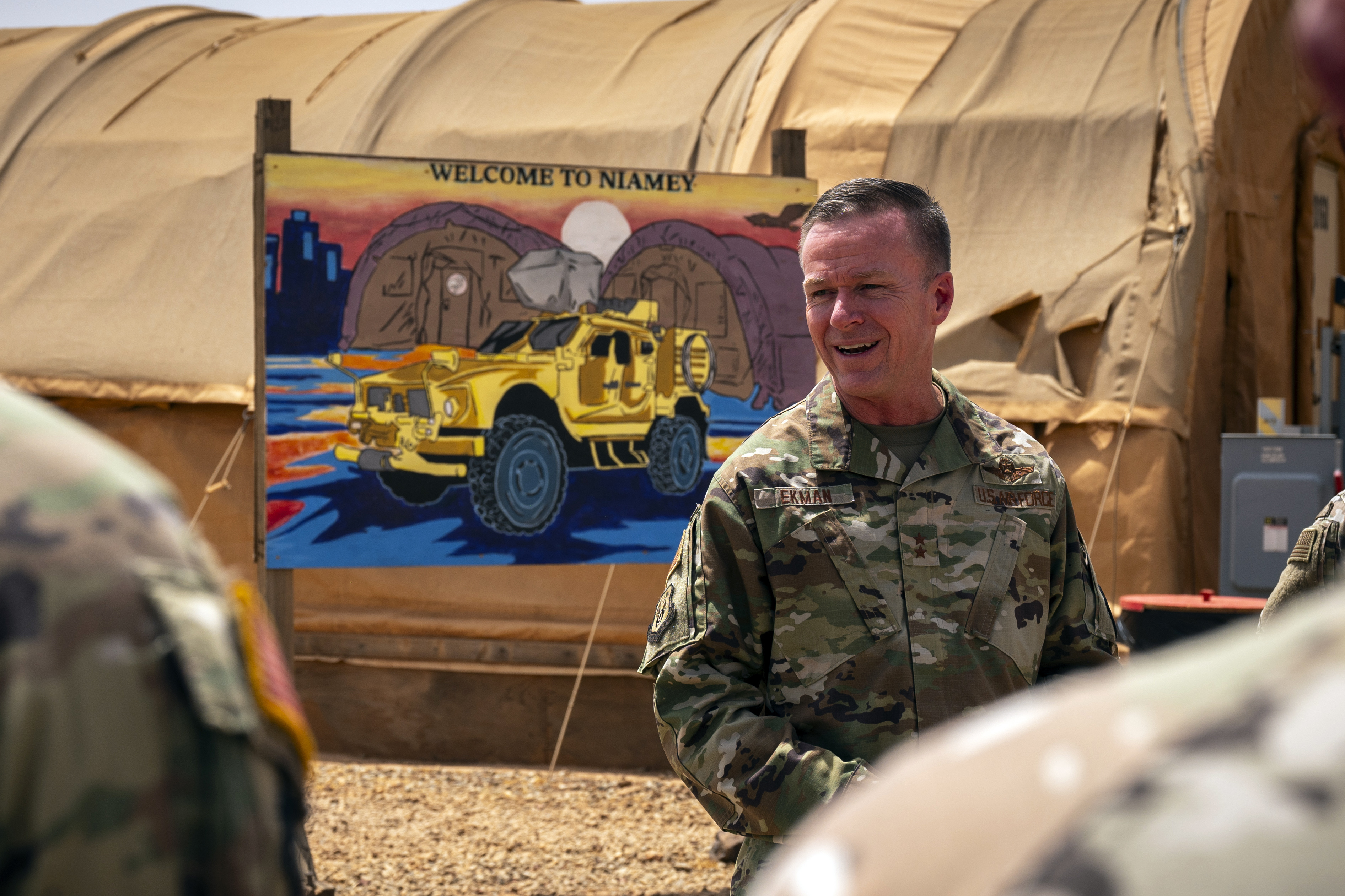 In this image by the U.S. Air Force, Maj. Gen. Kenneth P. Ekman speaks in front of a "Welcome to Niamey" sign depicting U.S. military vehicles at Air Base 101 in Niger, May 30, 2024. Ekman the U.S. military commander in Niger, says all American forces and equipment will leave a smaller base in the West African country this weekend and fewer than 500 remaining troops will be out of a critical drone base in August. (Tech. Sgt. Christopher Dyer, U.S. Air Force via AP)