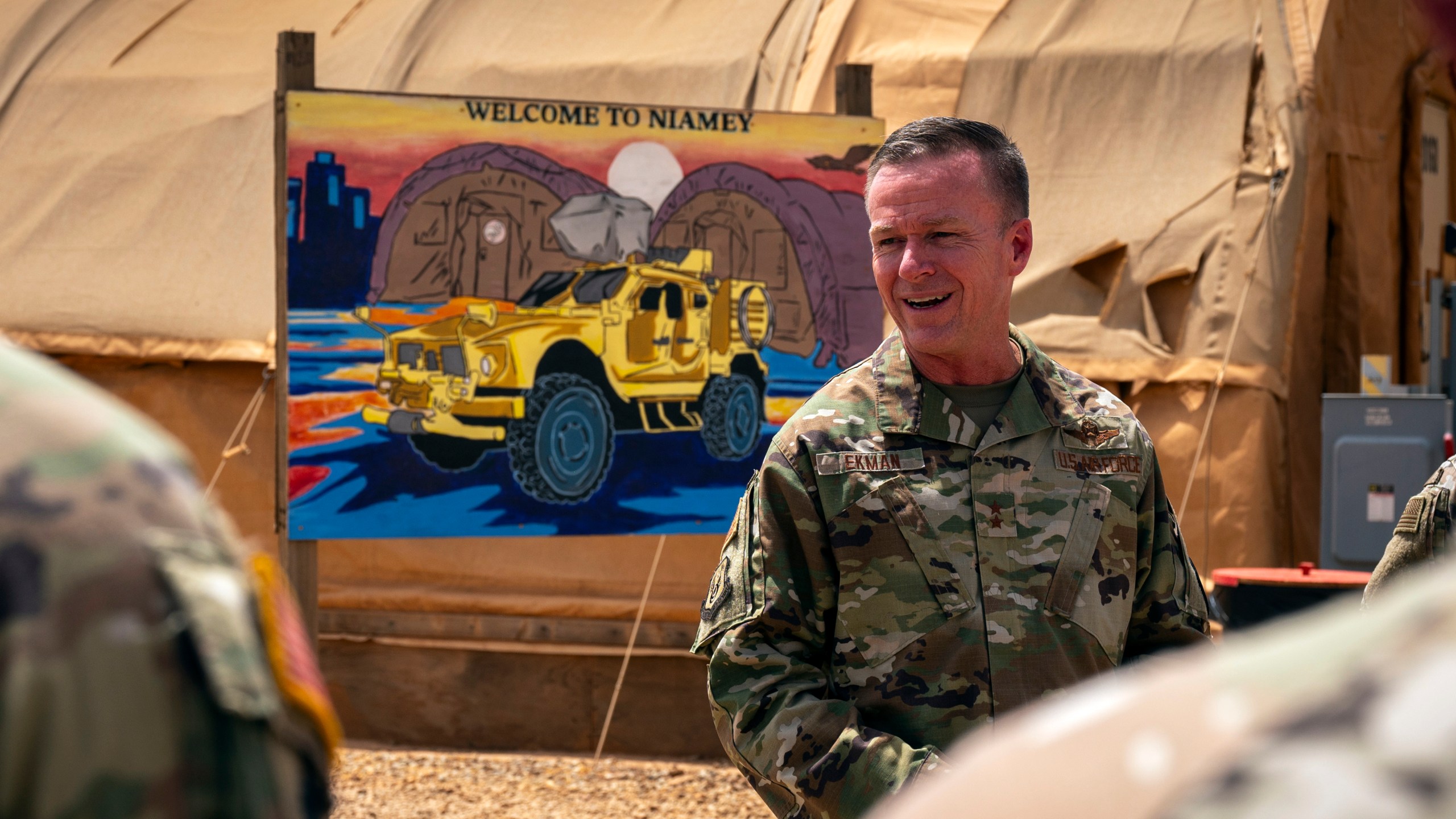 In this image by the U.S. Air Force, Maj. Gen. Kenneth P. Ekman speaks in front of a "Welcome to Niamey" sign depicting U.S. military vehicles at Air Base 101 in Niger, May 30, 2024. Ekman the U.S. military commander in Niger, says all American forces and equipment will leave a smaller base in the West African country this weekend and fewer than 500 remaining troops will be out of a critical drone base in August. (Tech. Sgt. Christopher Dyer, U.S. Air Force via AP)