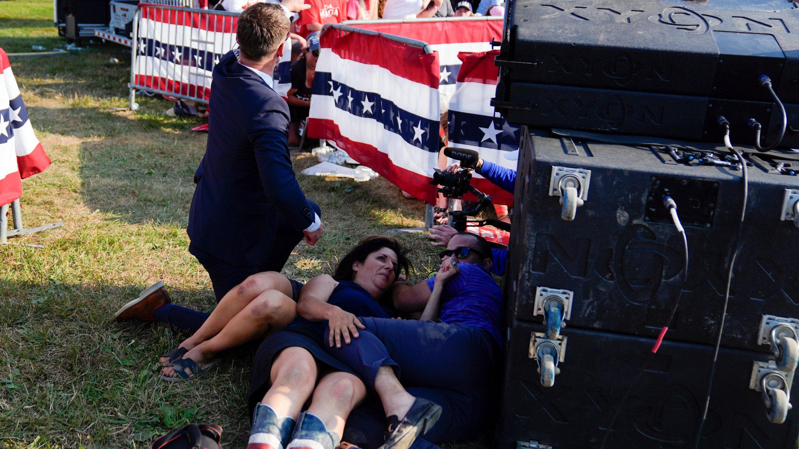 People take cover as U.S. Secret Service agents surround Republican presidential candidate former President Donald Trump on stage at a campaign rally, Saturday, July 13, 2024, in Butler, Pa. (AP Photo/Evan Vucci)