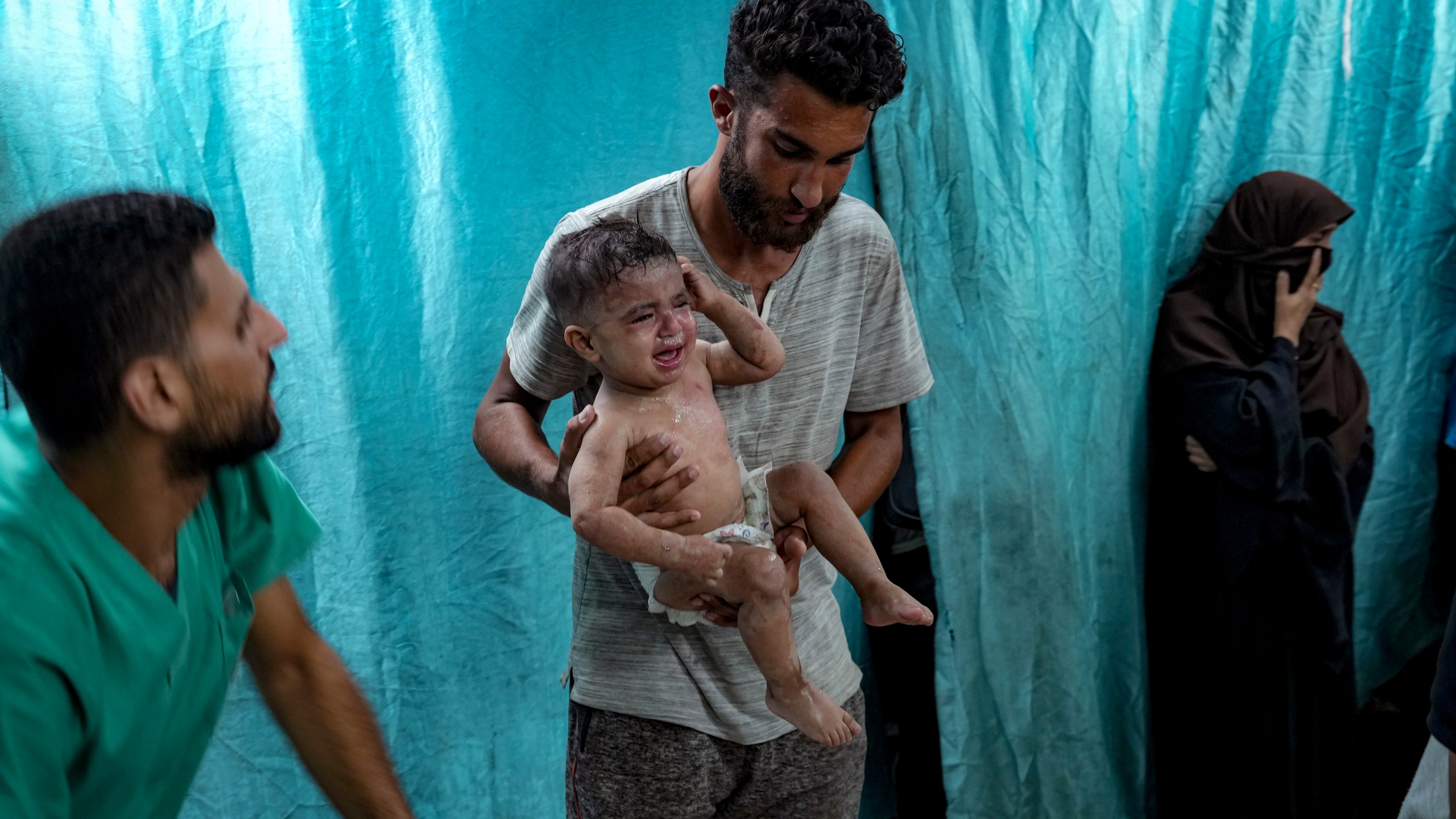 A Palestinian man holds a child wounded in the Israeli bombardment of the Gaza Strip in a hospital in Deir al-Balah, Thursday, July 18, 2024. (AP Photo/Abdel Kareem Hana)