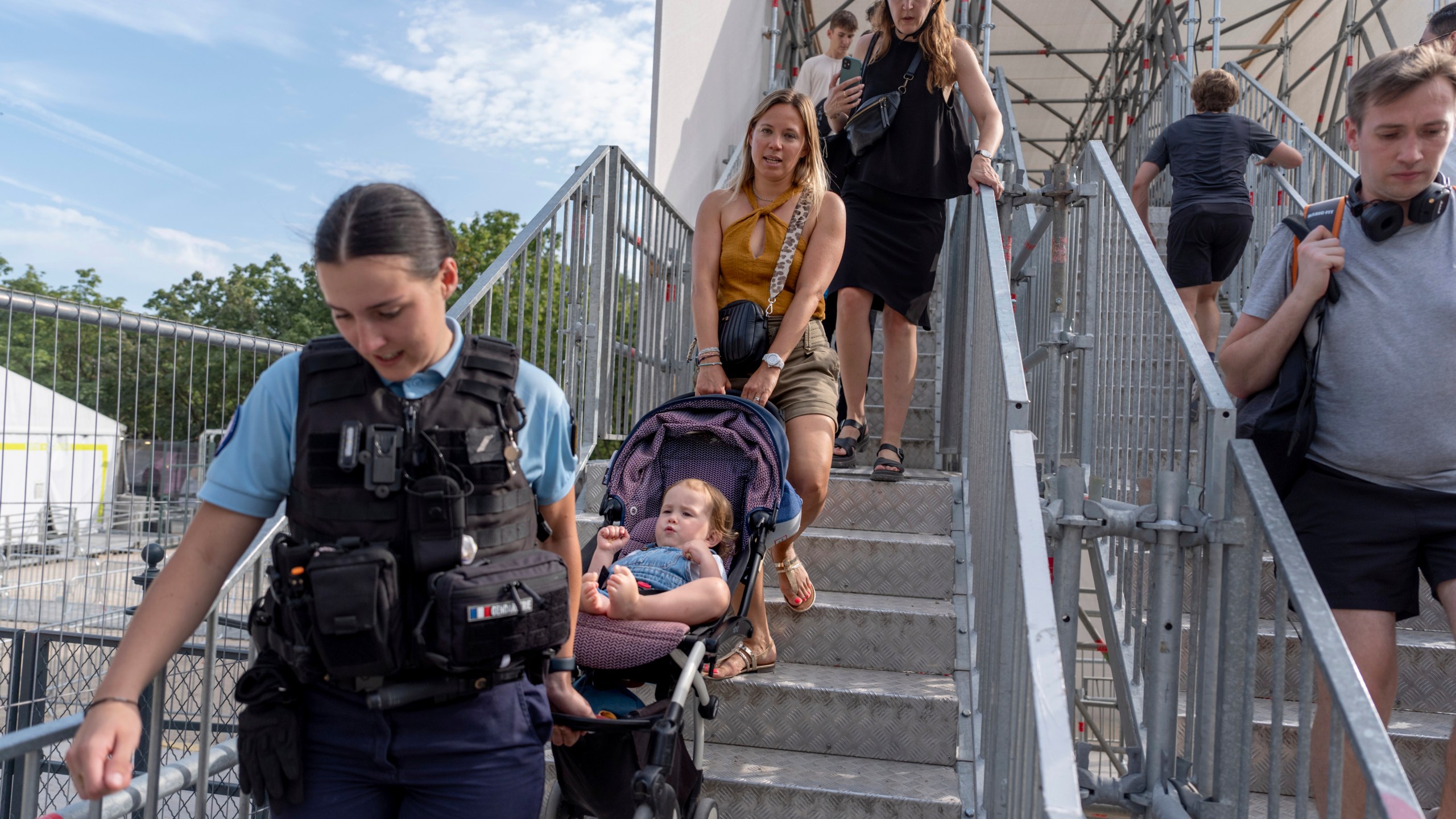 Severine Hiver, right, gets help from officer Romane Rouseel to carry her daughter, Sacha, 2, down a staircase in her stroller while navigating around a security area closed off for the 2024 Summer Olympics, Thursday, July 18, 2024, in Paris. A special kind of iron curtain came down across central Paris on Thursday, with the beginning of an Olympic anti-terrorism perimeter along the banks of the River Seine sealing off a kilometers-long (miles-long) area to Parisians and tourists who hadn't applied in advance for a pass. (AP Photo/David Goldman)