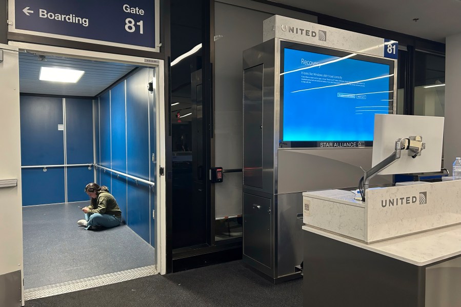 A traveler at Los Angeles International Airport sits in a jetway for a delayed United Airlines flight to Dulles International Airport due to a widespread global technology outage disrupting flights, banks, media outlets and companies around the world, Friday, July 19, 2024, in Los Angeles. (AP Photo/Stefanie Dazio)