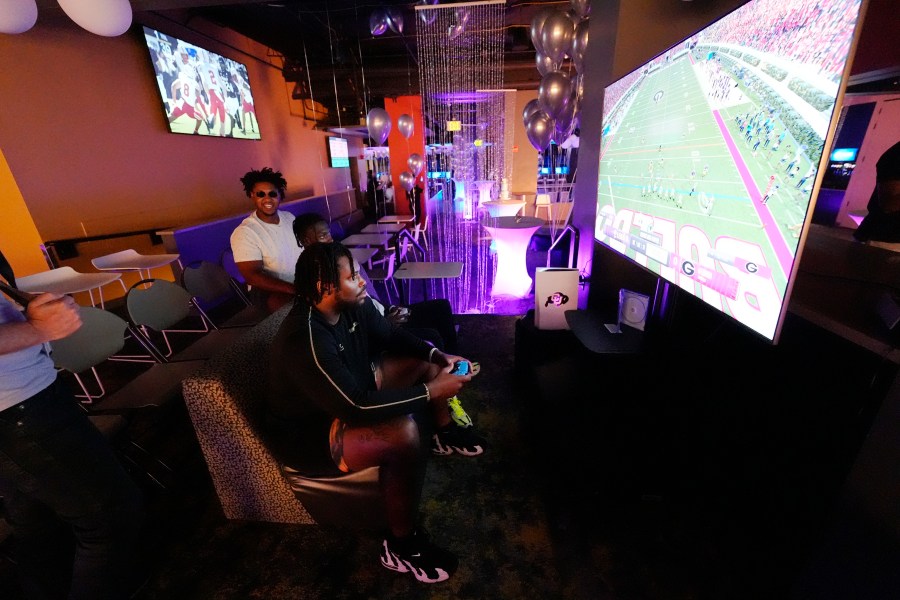 Colorado center Yakiri Walker, front, and running back Kam Mikell, center, join offensive lineman Tyler Johnson, left, in playing the EA Sports College Football 25 video game during a release party Friday, July 19, 2024, at the Memorial Union on the campus of the University of Colorado in Boulder, Colo. EA Sports College Football 25 flooded the market Friday as gamers who waited more than a decade for the franchise's next installment hurry to play. (AP Photo/David Zalubowski)