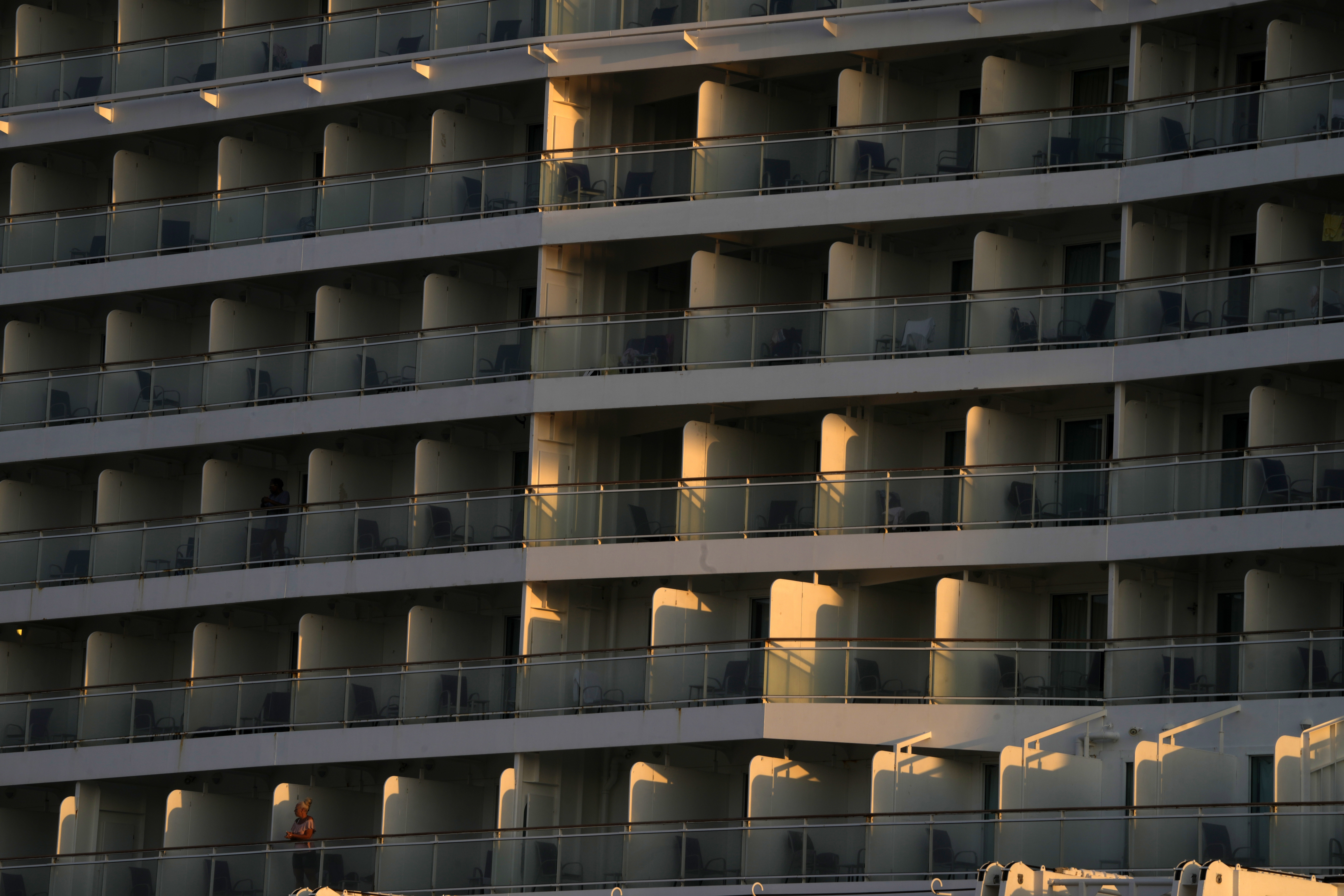A woman, bottom left, stands on the balcony of a cruise ship which is docked at Athens' port city of Piraeus, as the sun rises on Monday, July 22, 2024. The heatwave continues in Greece, with temperatures hovering at 40 degrees Celsius (104 Fahrenheit) in several places, but the meteorologists expecting to slight drop from tomorrow. (AP Photo/Thanassis Stavrakis)