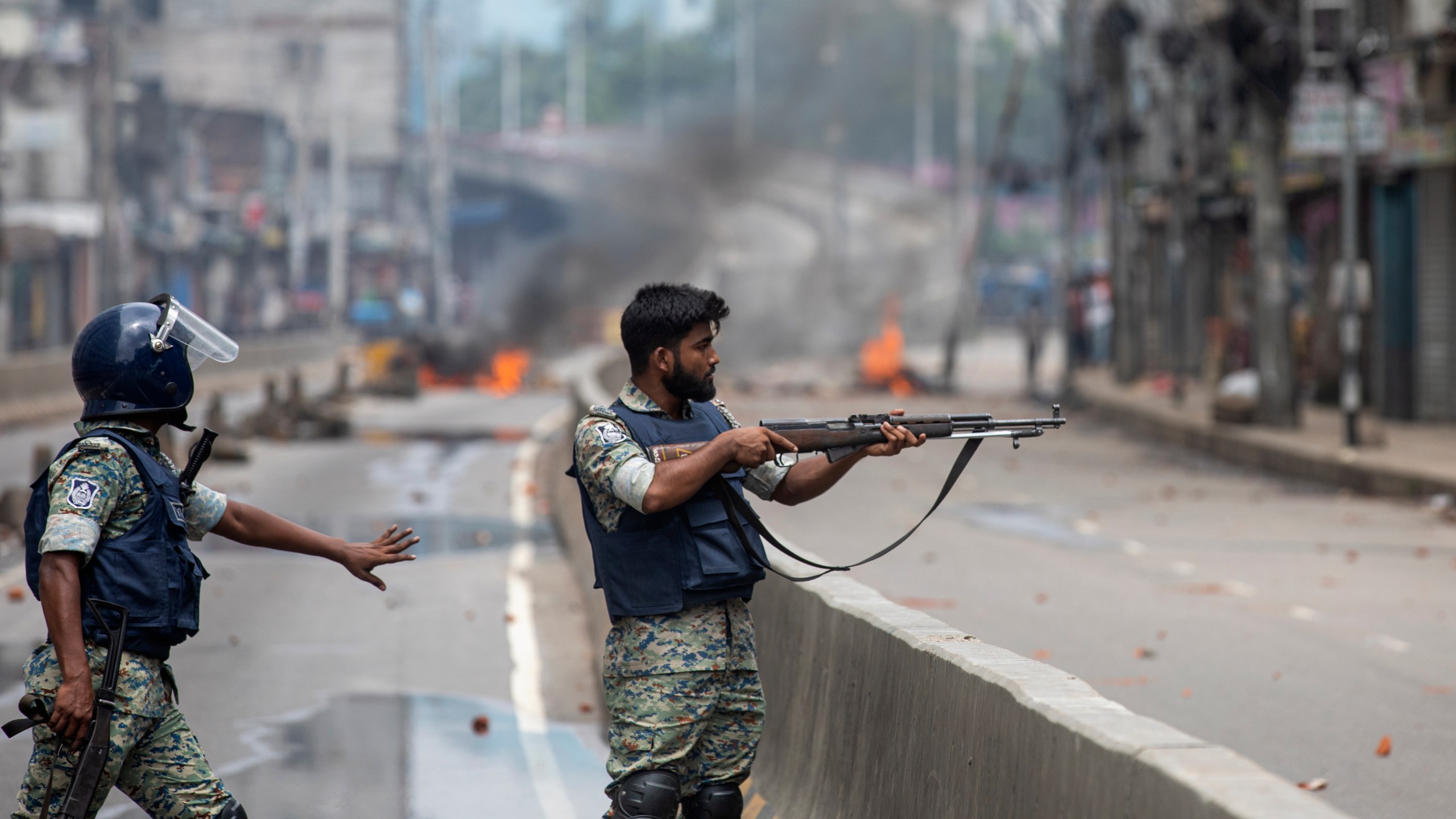 FILE- A policeman aims his weapon at protesters during a curfew imposed following violence during protests against Prime Minister Sheikh Hasina and her government, in Dhaka, Bangladesh, Aug. 5, 2024. (AP Photo/Rajib Dhar, File)