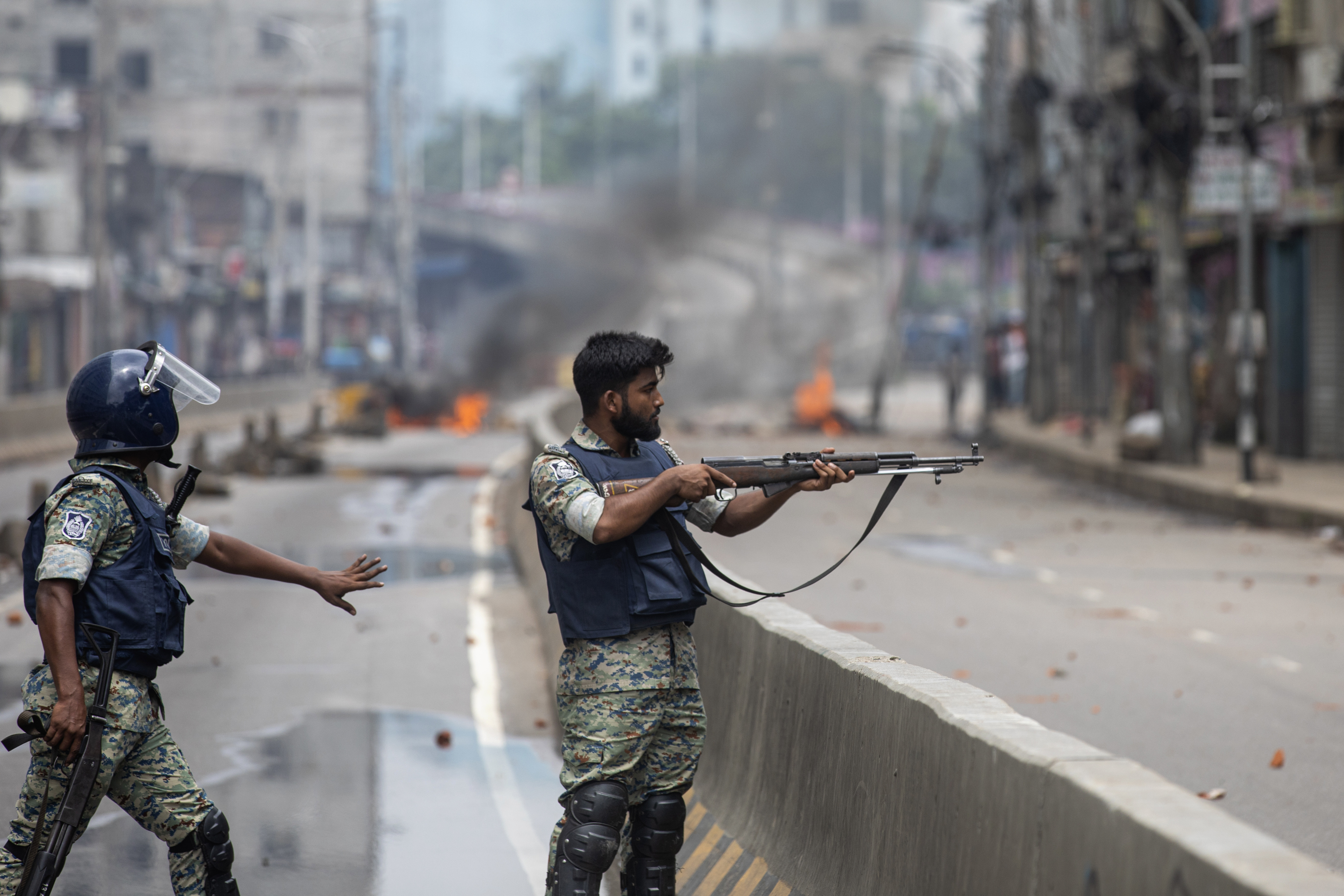 FILE- A policeman aims his weapon at protesters during a curfew imposed following violence during protests against Prime Minister Sheikh Hasina and her government, in Dhaka, Bangladesh, Aug. 5, 2024. (AP Photo/Rajib Dhar, File)