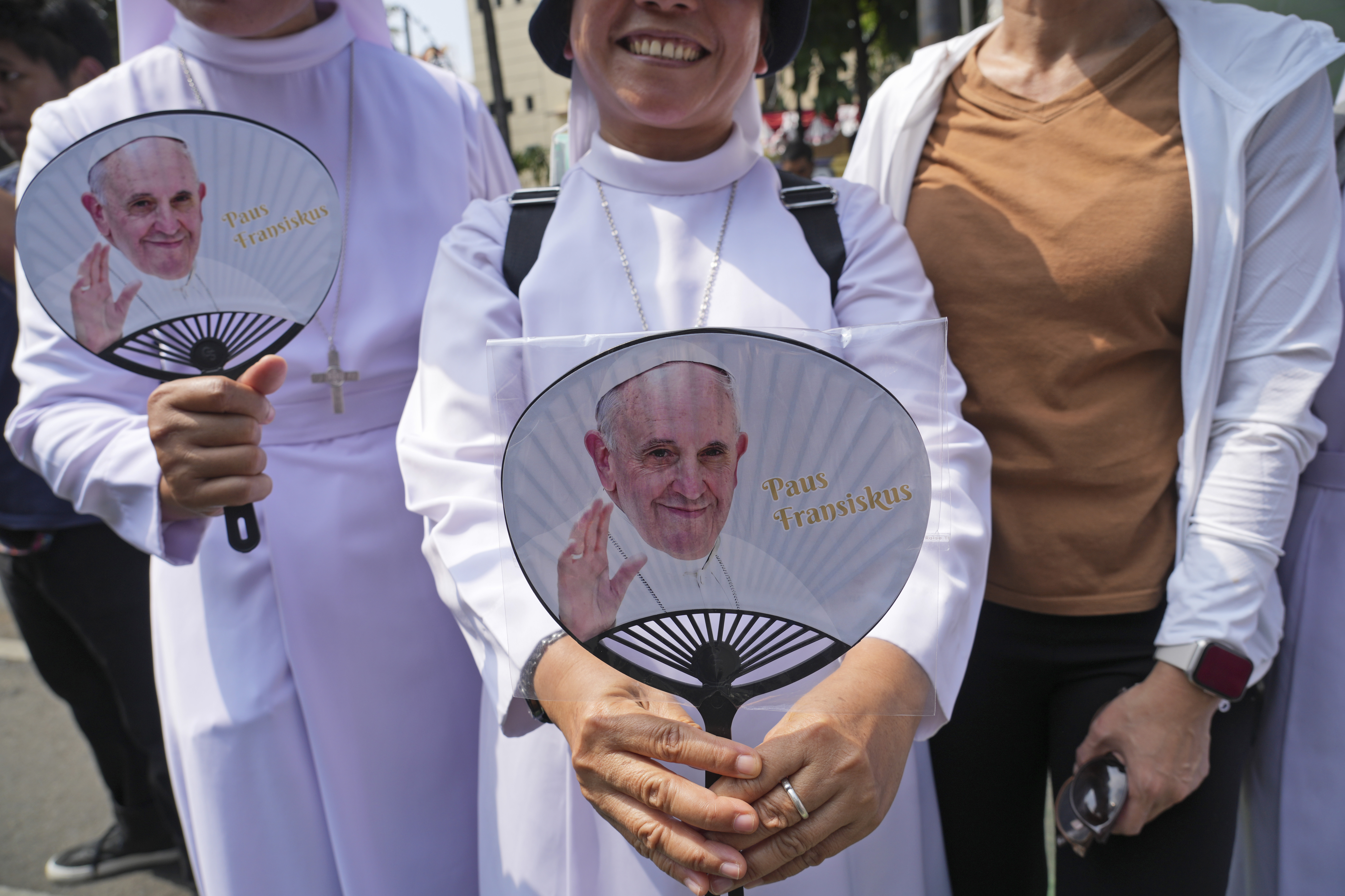 Devotees carrying hand fans printed with portraits of Pope Francis wait outside the Indonesian Bishops' Conference Headquarters to welcome the pope before his arrival for a meeting, in Jakarta, Indonesia, Thursday, Sept. 5, 2024. (AP Photo/ Tatan Syuflana)