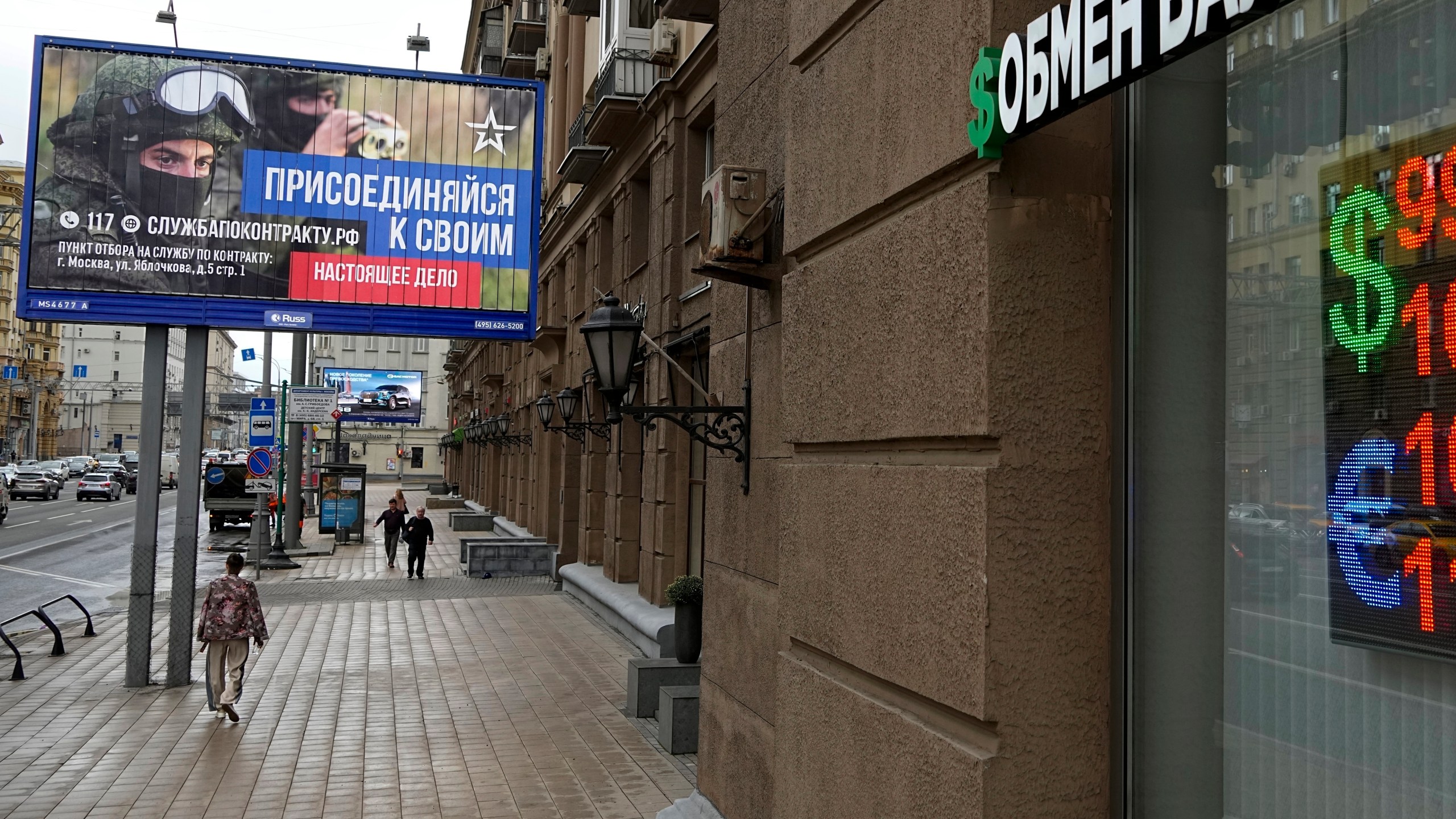 FILE - People walk past a currency exchange office with an army recruiting billboard calling for a contract for service in the Russian armed forces in Moscow, Russia,on Aug. 14, 2023. (AP Photo, File)