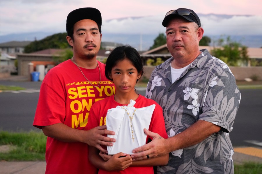 FILE - Briena Mae Rabang, 10, holds the ashes of her great-grandmother Sharlene Rabang, who was named as the 100th victim of the Lahaina wildfire, while posing for a photo with her father Branden, left, and grandfather Brandon, right, Friday, Dec. 8, 2023, in Kahului, Hawaii. (AP Photo/Lindsey Wasson, File)