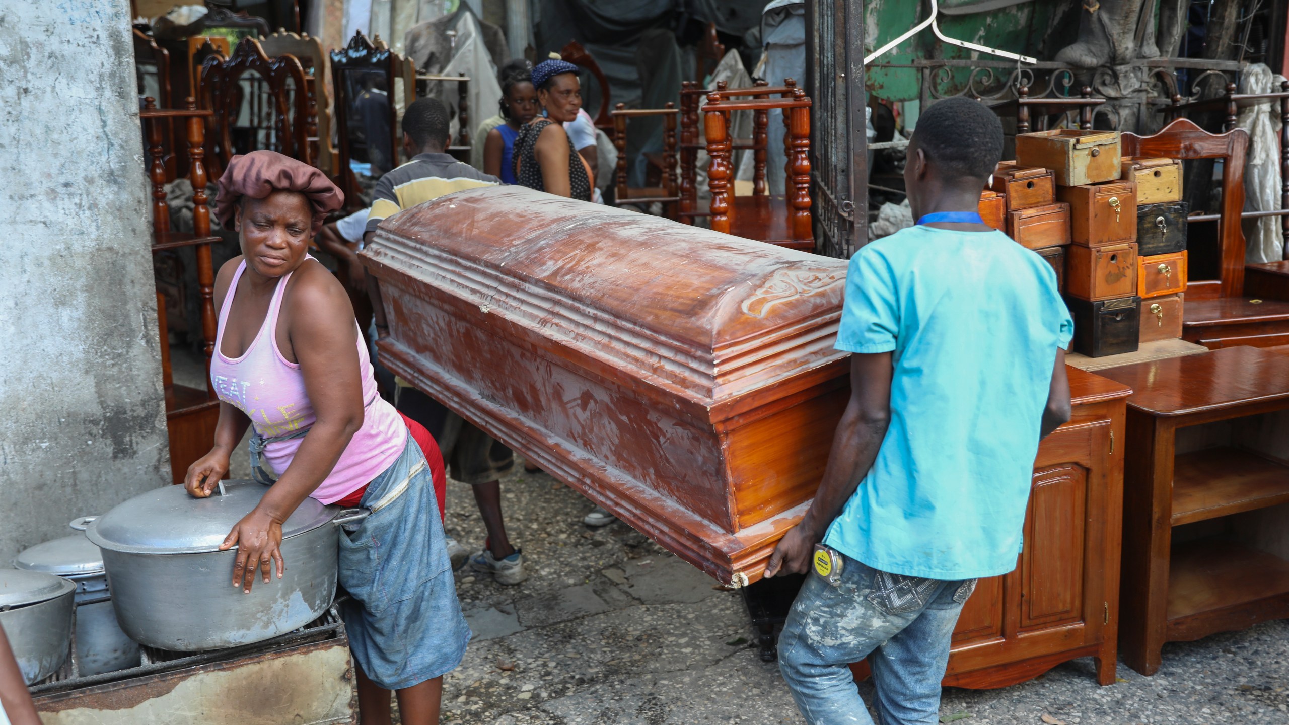 People carry an empty coffin past a street food vendor into the shop that is buying it to repair and sell in Port-au-Prince, Haiti, Friday, Sept. 13, 2024. (AP Photo/Odelyn Joseph)