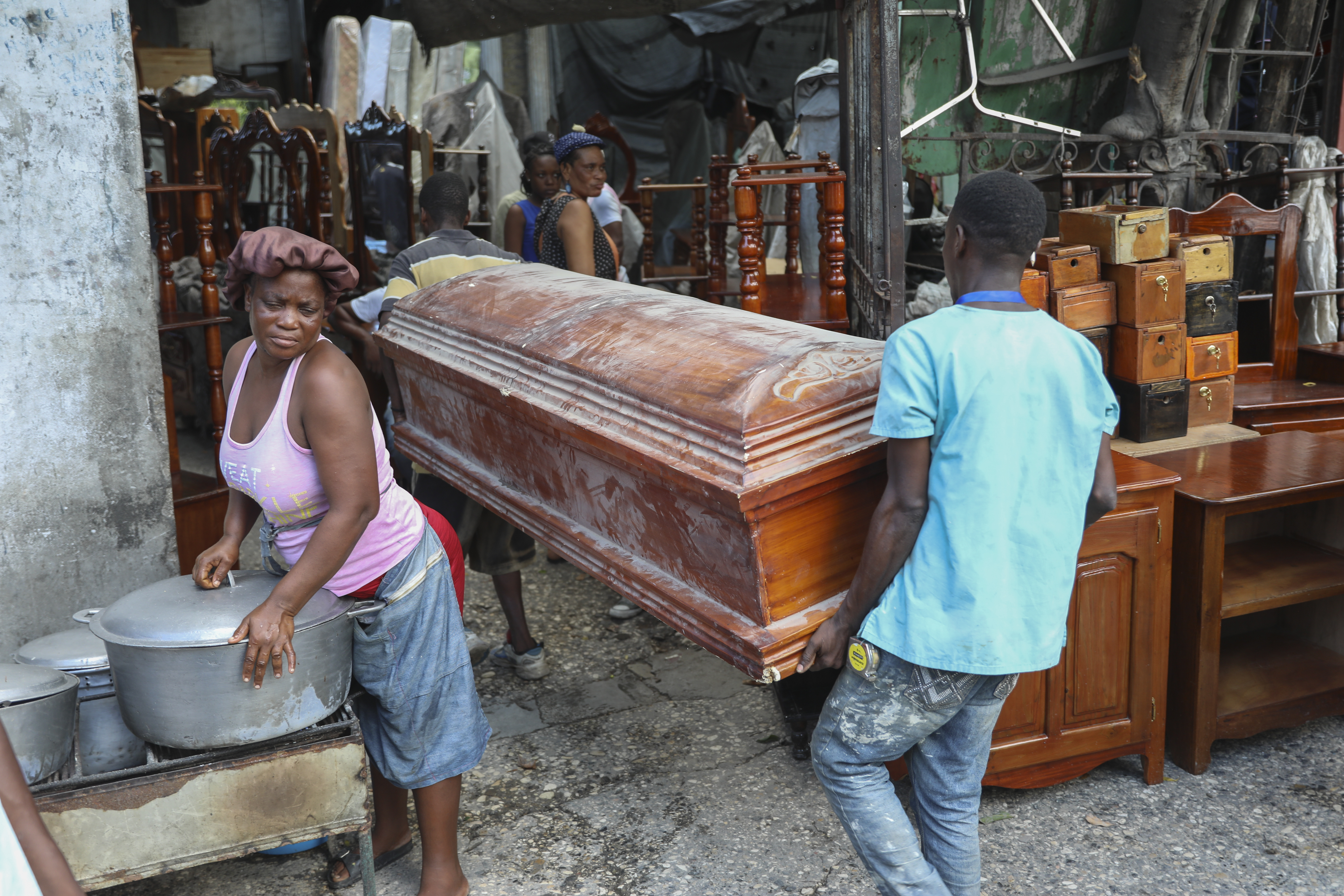 People carry an empty coffin past a street food vendor into the shop that is buying it to repair and sell in Port-au-Prince, Haiti, Friday, Sept. 13, 2024. (AP Photo/Odelyn Joseph)