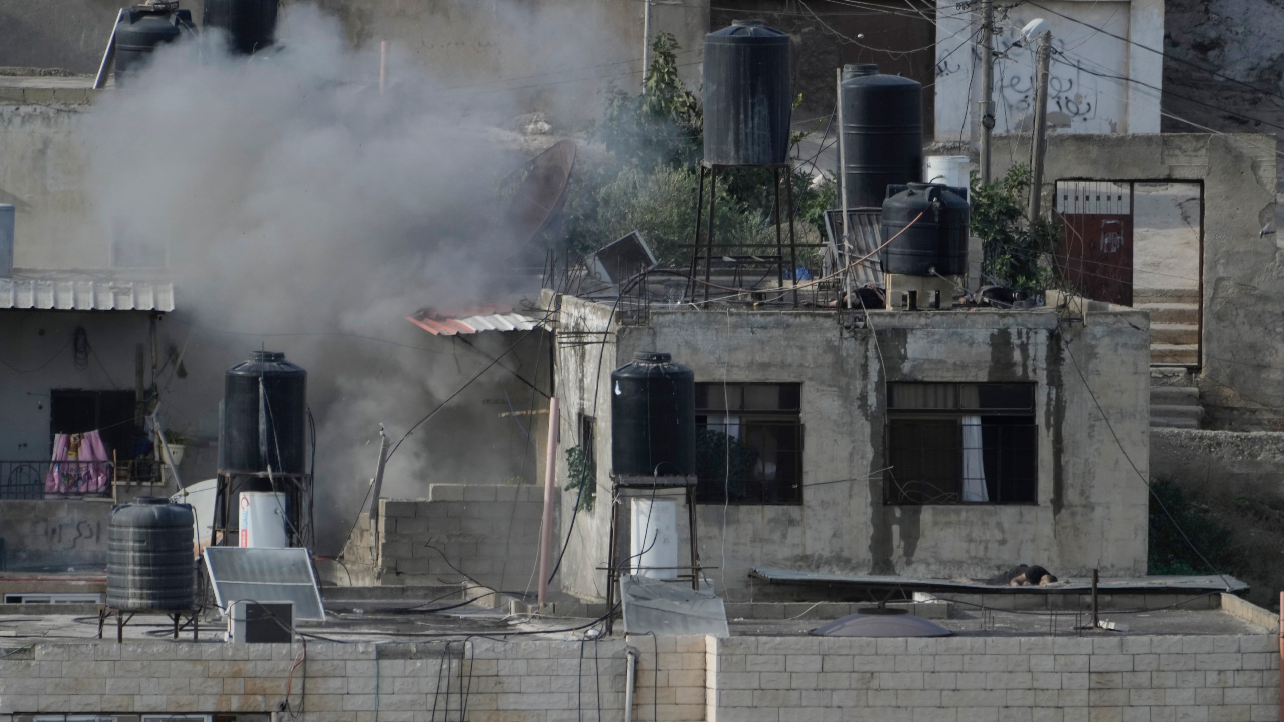 EDS NOTE: GRAPHIC CONTENT - An explosion is seen as three bodies lie motionless on rooftops in the West Bank town of Qabatiya during a raid, Thursday, Sept. 19, 2024. (AP Photo/Majdi Mohammed)