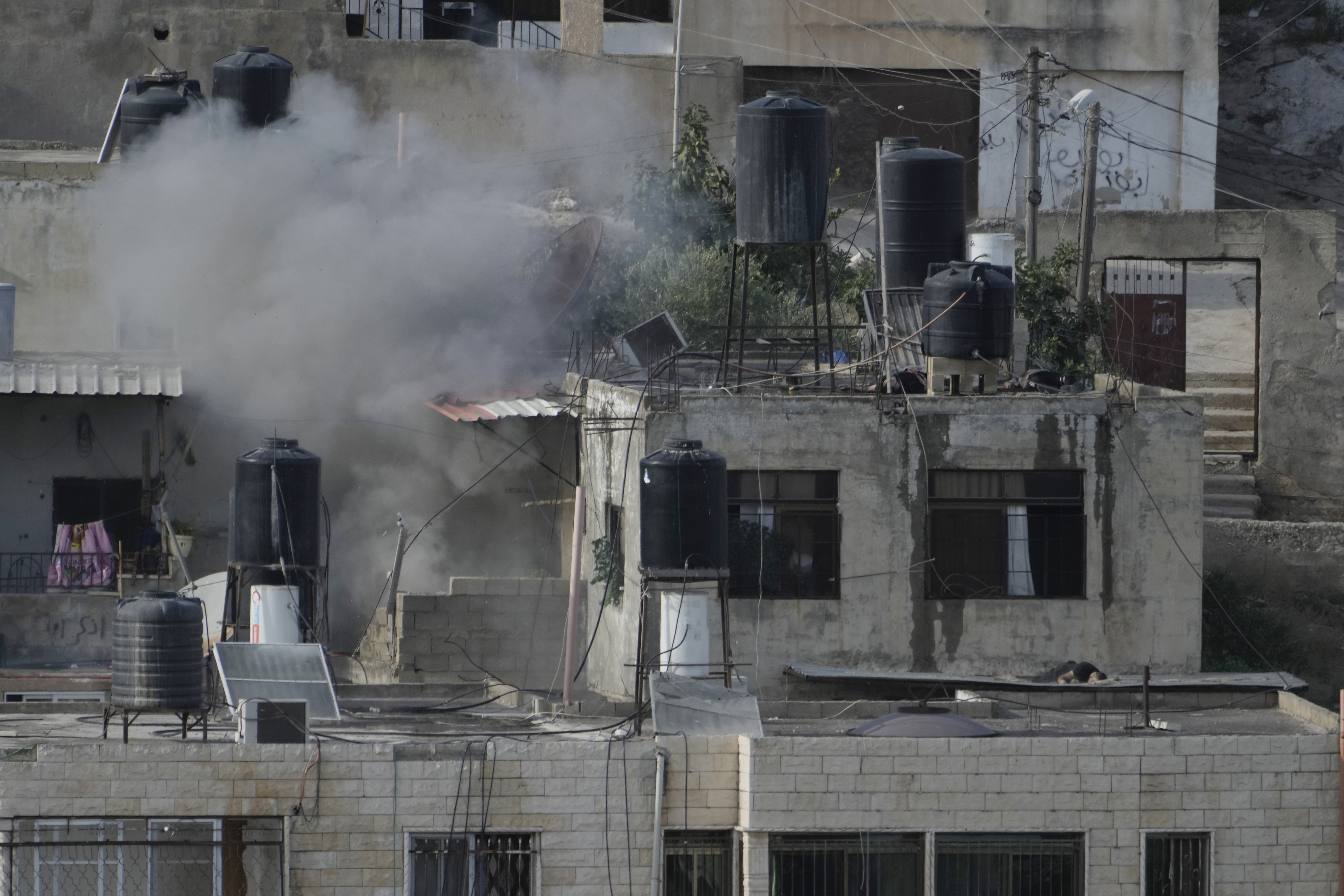 EDS NOTE: GRAPHIC CONTENT - An explosion is seen as three bodies lie motionless on rooftops in the West Bank town of Qabatiya during a raid, Thursday, Sept. 19, 2024. (AP Photo/Majdi Mohammed)