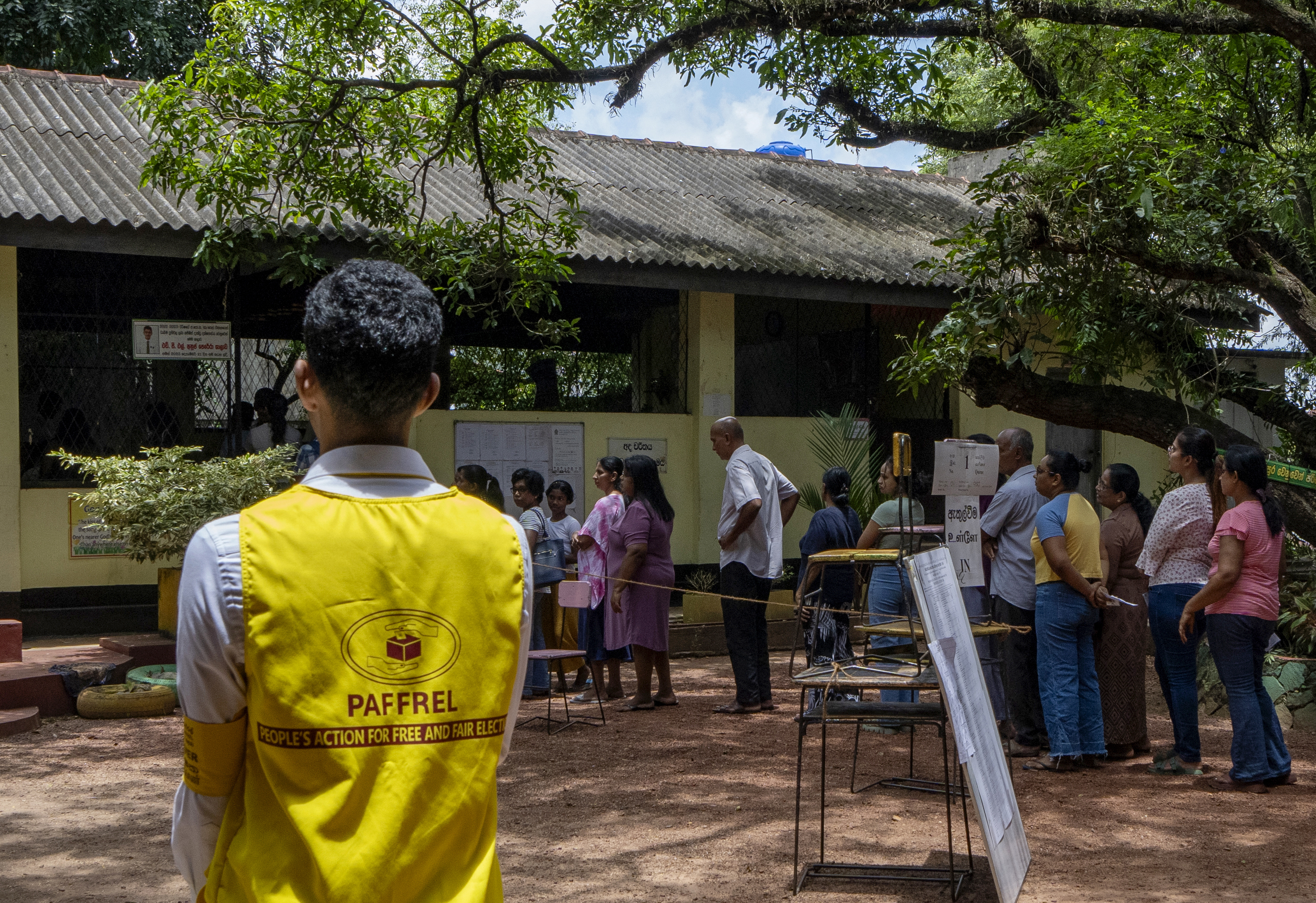 An election monitor watches voters waiting in queue at a polling center during the presidential election on the outskirts of Colombo, Sri Lanka Saturday, Sept. 21, 2024.(AP Photo/Rajesh Kumar Singh)