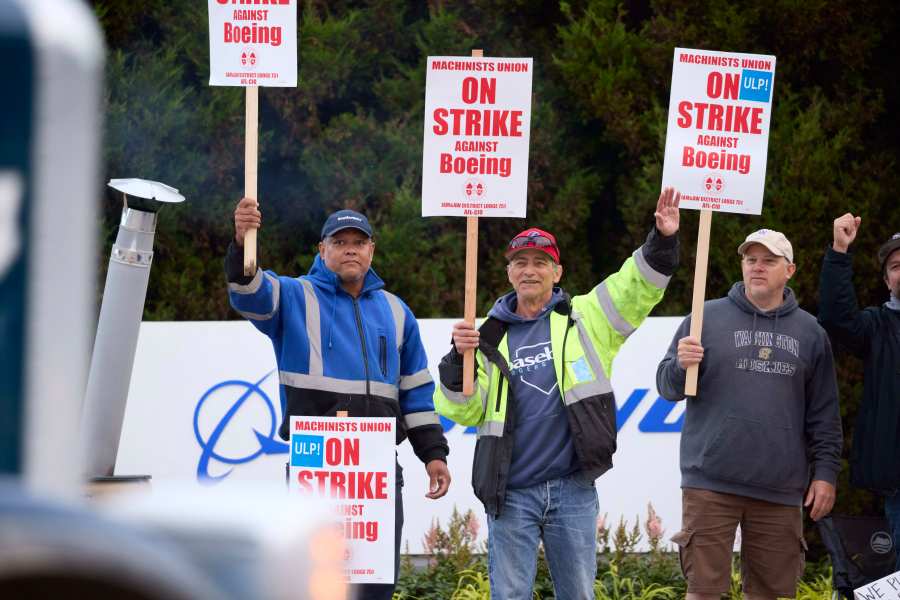 Boeing Machinists Union members Steven Wilson, left, Dave Hendrickson, center,, and Mark Erickson, right, wave to passing traffic while on the picket line at the Renton assembly plant, Friday, Sept. 13, 2024, in Renton, Wash. (AP Photo/John Froschauer)