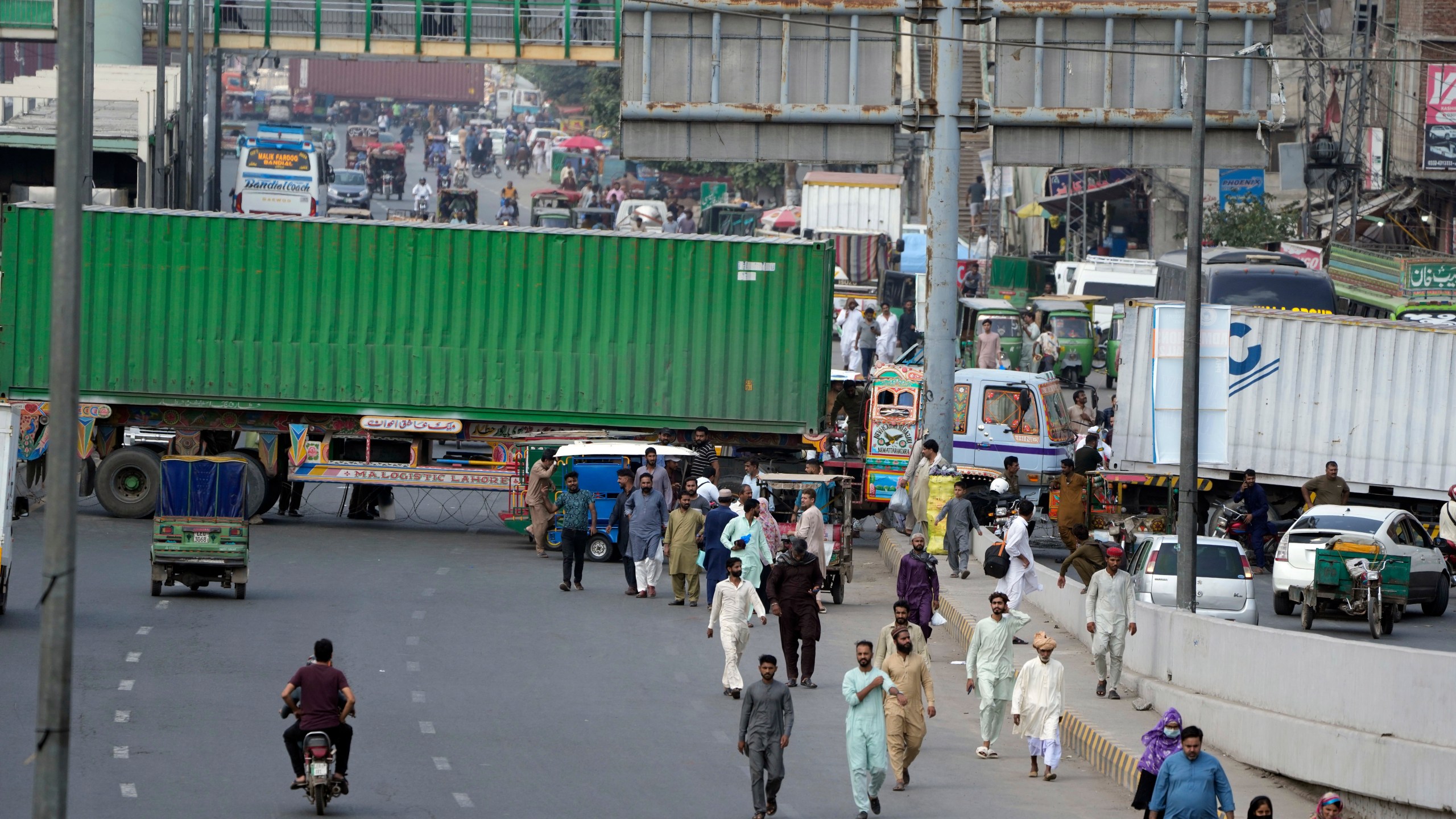 People try to cross through shipping containers set up by authorities to prevent supporters of imprisoned former Prime Minister Imran Khan from holding a rally to demand his release in Lahore, Pakistan, Saturday, Oct. 5, 2024. (AP Photo/K.M. Chaudary)