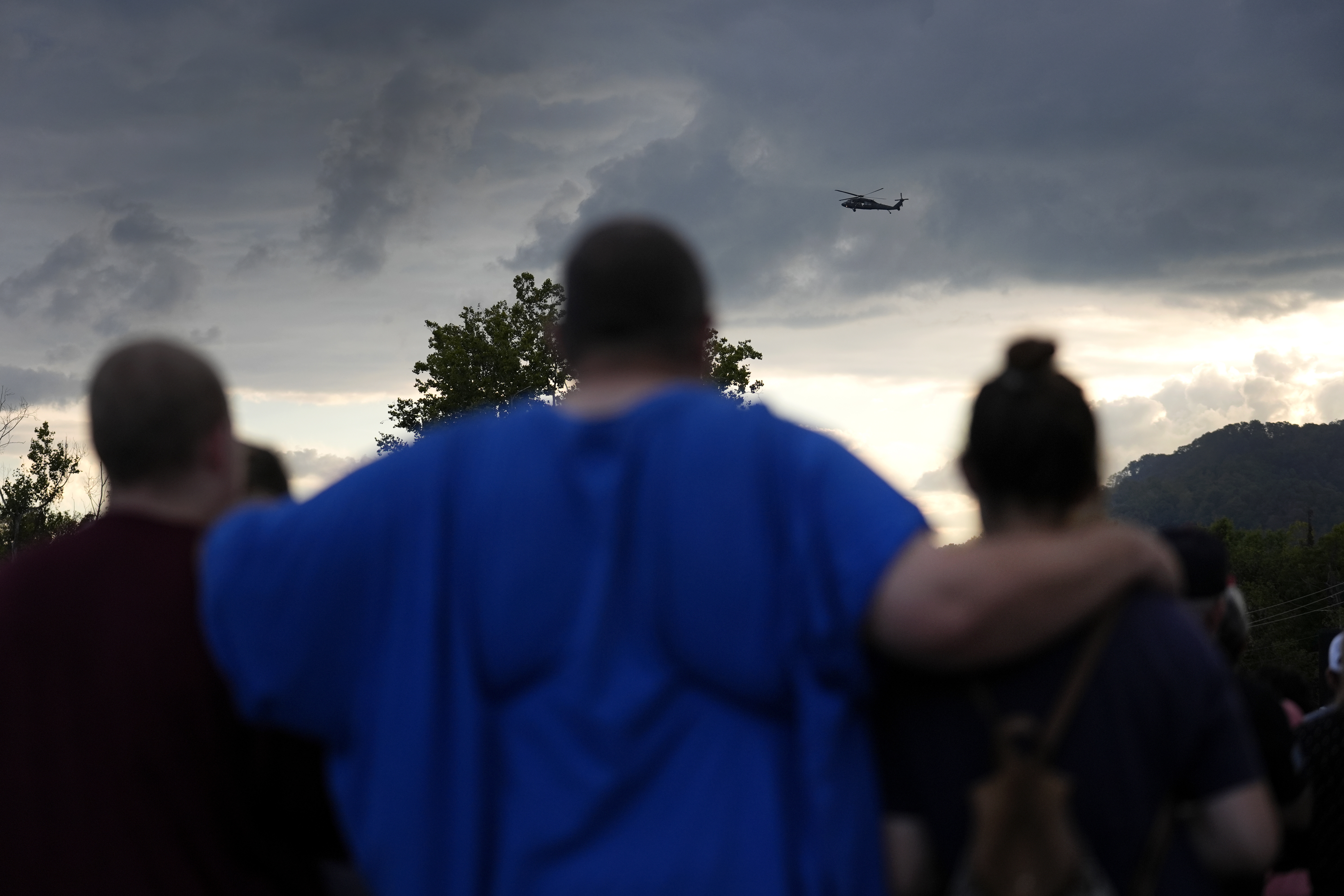 Mourners gather during a vigil for victims of the Impact Plastics tragedy as a helicopter continues search and rescue work over the disaster site in the distance in the days after Hurricane Helene in Erwin, Tenn., on Thursday, Oct. 3, 2024. (AP Photo/Jeff Roberson)