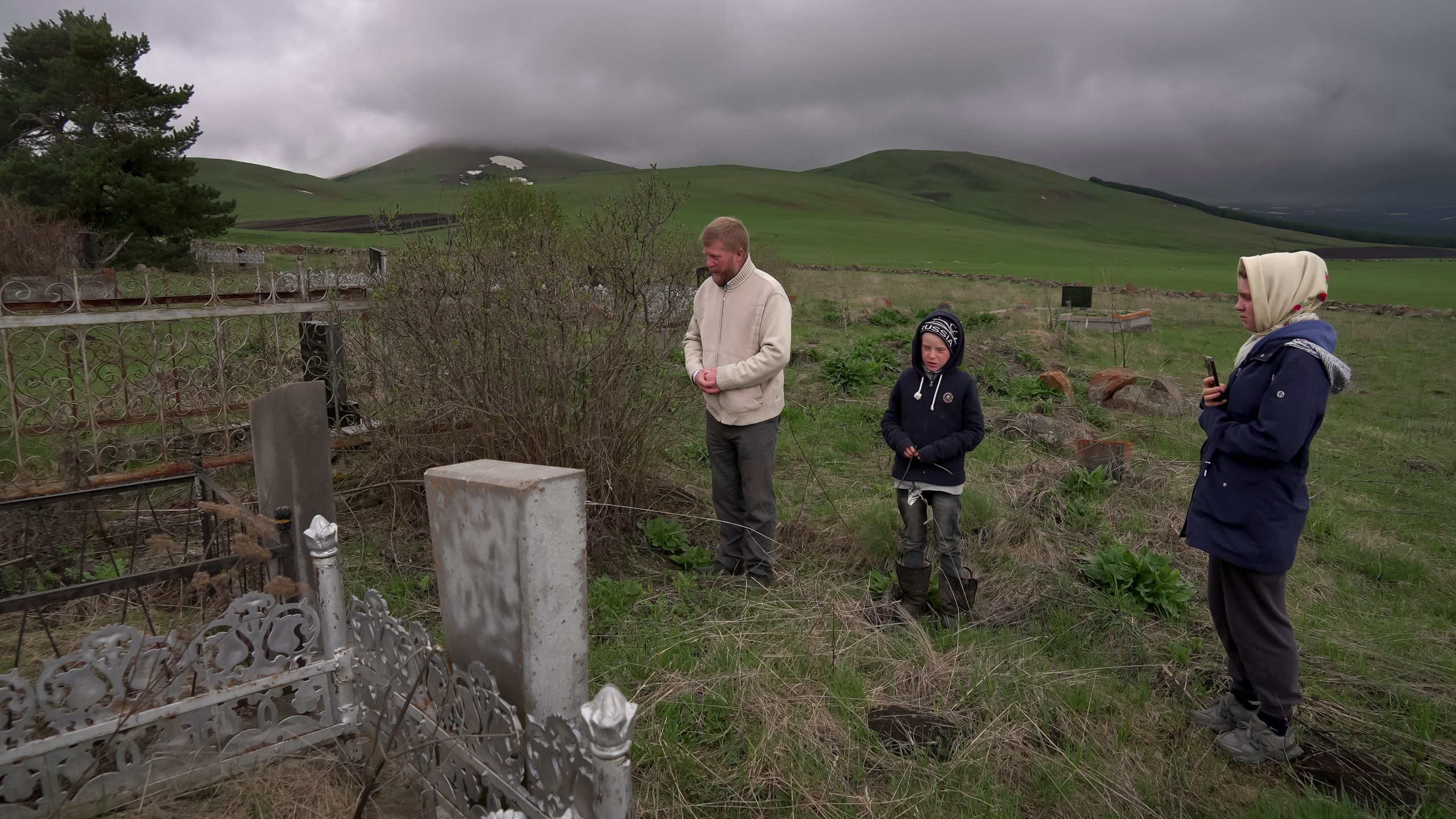 Yuri Strukov, 46, his son Ilya, 10, and his daughter Daria, 21, pray at the Doukhobor cemetery outside of the remote mountain village of Orlovka, Georgia, Saturday, May 4, 2024. (AP Photo/Kostya Manenkov)