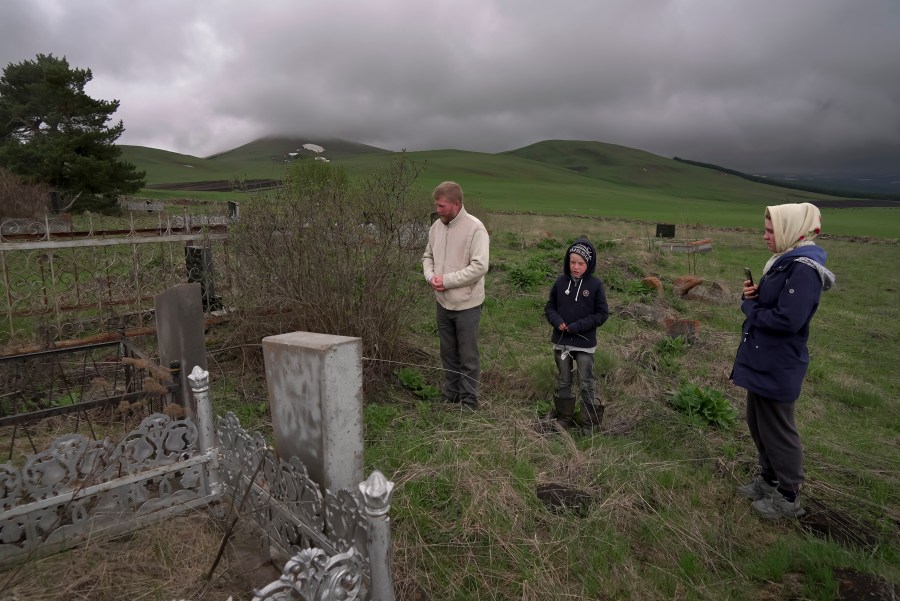 Yuri Strukov, 46, his son Ilya, 10, and his daughter Daria, 21, pray at the Doukhobor cemetery outside of the remote mountain village of Orlovka, Georgia, Saturday, May 4, 2024. (AP Photo/Kostya Manenkov)