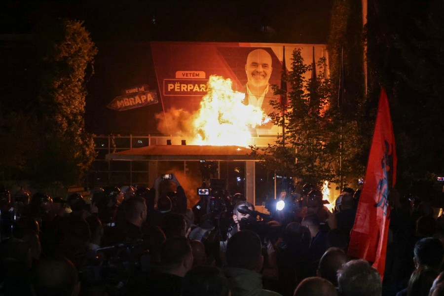 Fire burns behind a riot police cordon and in front of a poster depicting the Albania Prime minister Edi Rama during an anti-government rally set up by the opposition, in Tirana, Albania, Monday, Oct. 7, 2024. (AP Photo/Hameraldi Agolli)