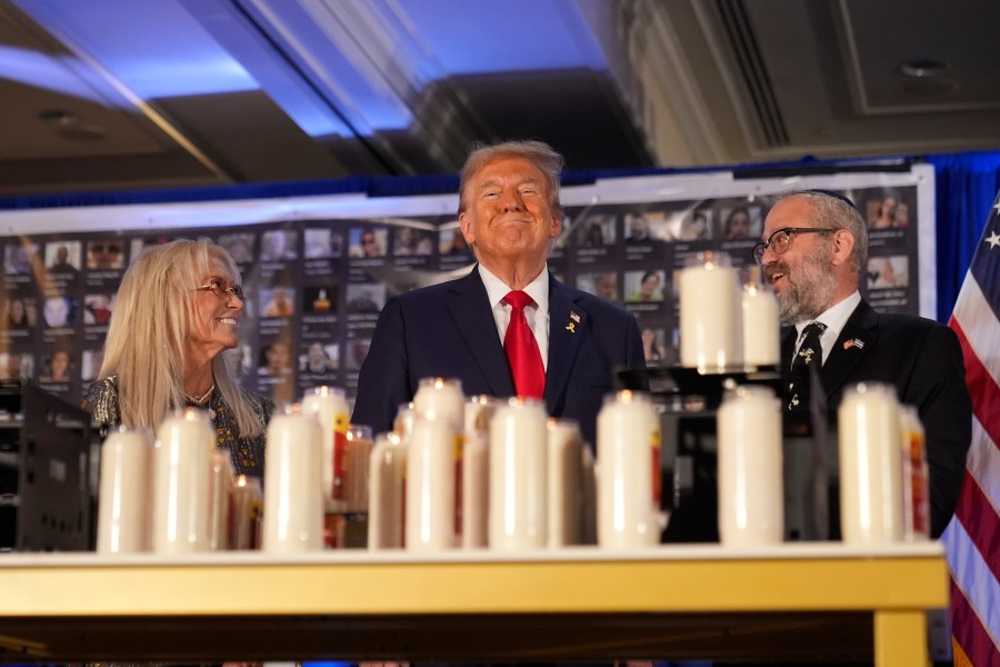 Republican presidential nominee former President Donald Trump stands with Miriam Adelson and Rabbi Yeshuda Kaploun at an event marking one year since the Oct. 7 Hamas attack on Israel, Monday, Oct. 7, 2024, in Miami. (AP Photo/Alex Brandon)