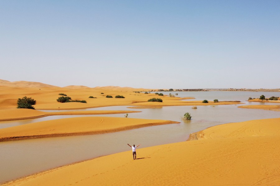 A man gestures as he walks on sand dunes next to a lake caused by heavy rainfall in the desert town of Merzouga, near Rachidia, southeastern Morocco, Wednesday, Oct. 2, 2024. (AP Photo)