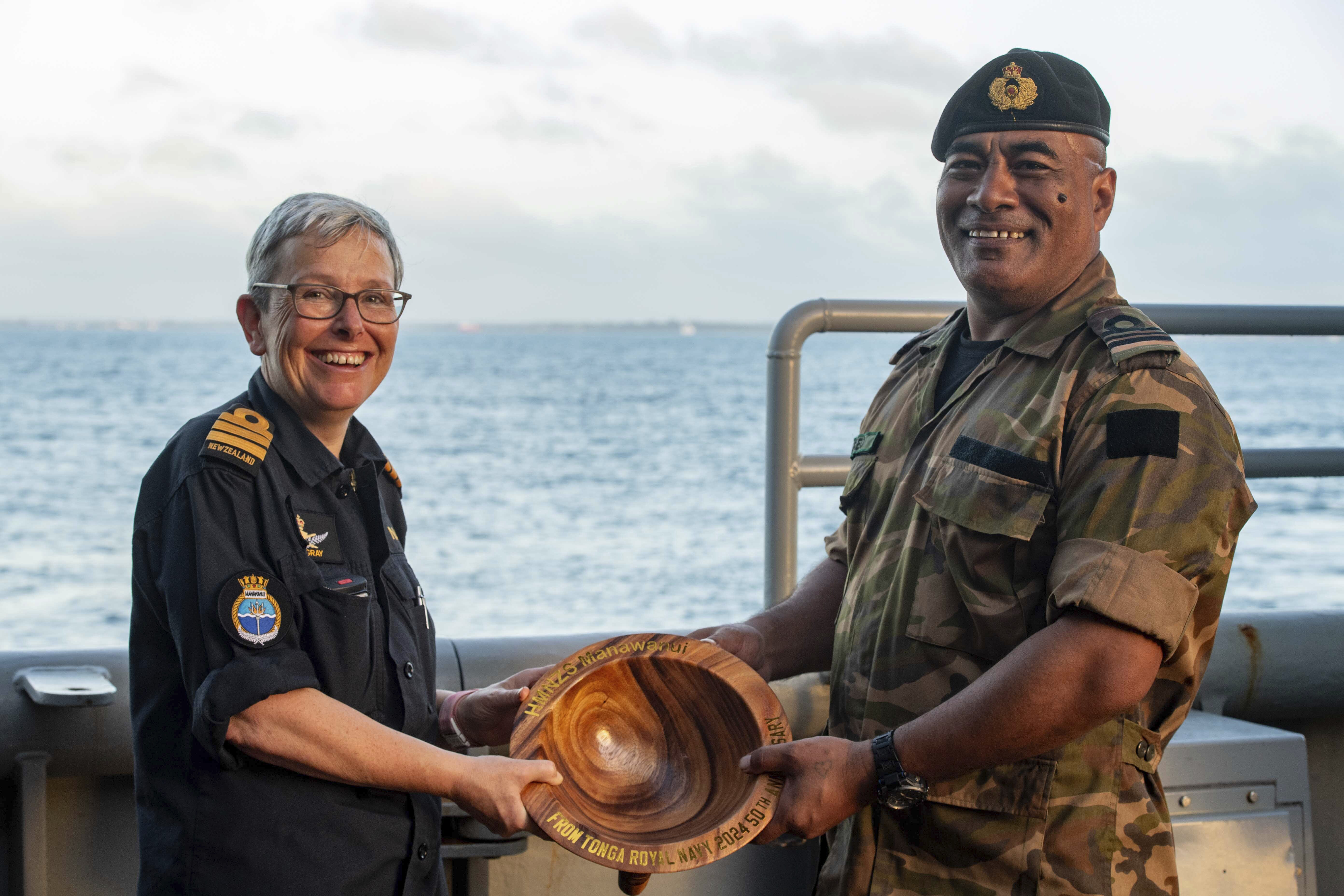 In this undated photo provided by the New Zealand Defence Force, Lieutenant Commander Tala Mafile'o of the Royal Tongan Navy presents Commander Yvonne Gray, left, with a carved wooden bowl as a memento of the RNZN's participation in the 50th Anniversary Fleet Review. (New Zealand Defence Force via AP)