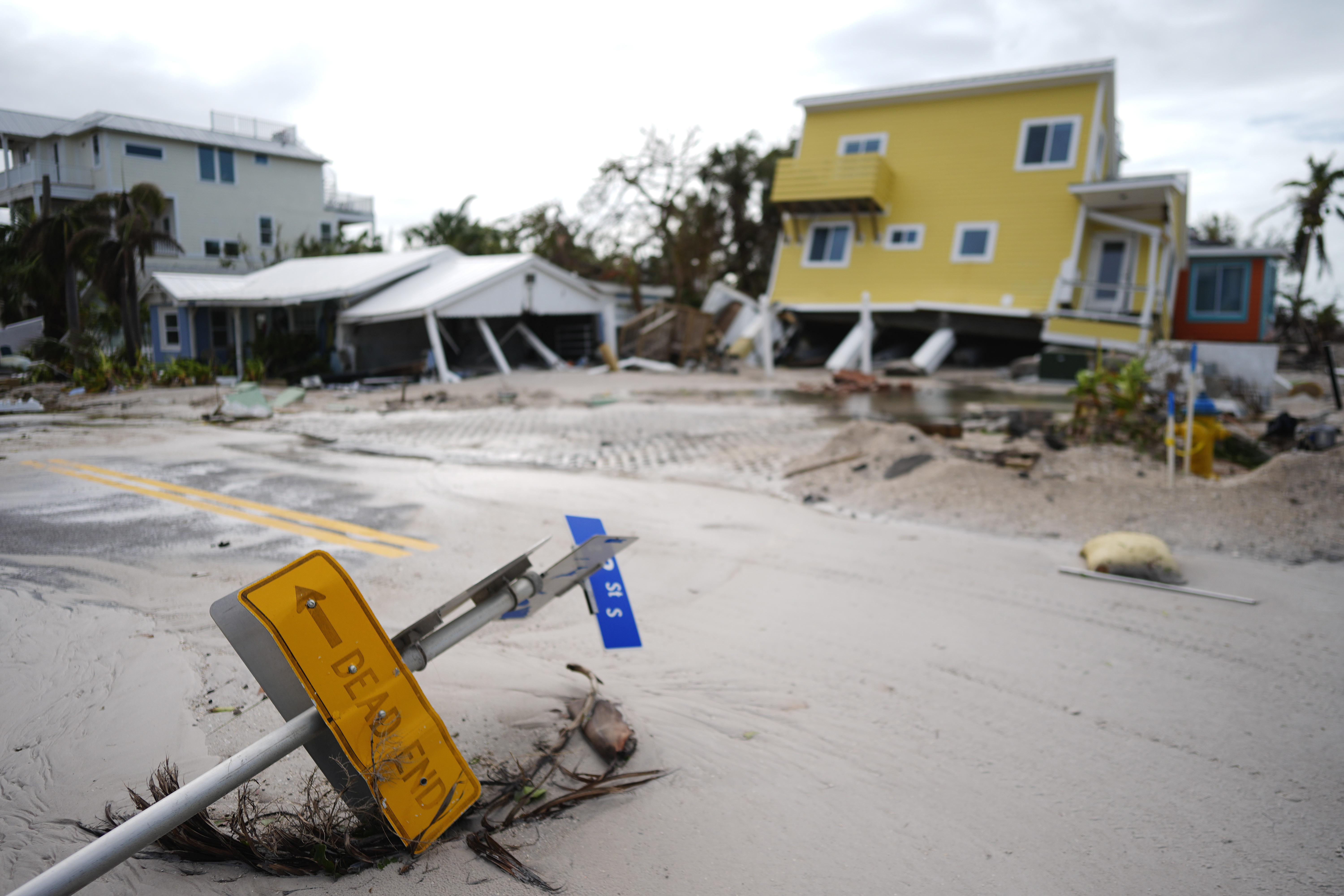 A house sits toppled off its stilts after the passage of Hurricane Milton, alongside an empty lot where a home was swept away by Hurricane Helene, in Bradenton Beach on Anna Maria Island, Fla., Thursday, Oct. 10, 2024. (AP Photo/Rebecca Blackwell)