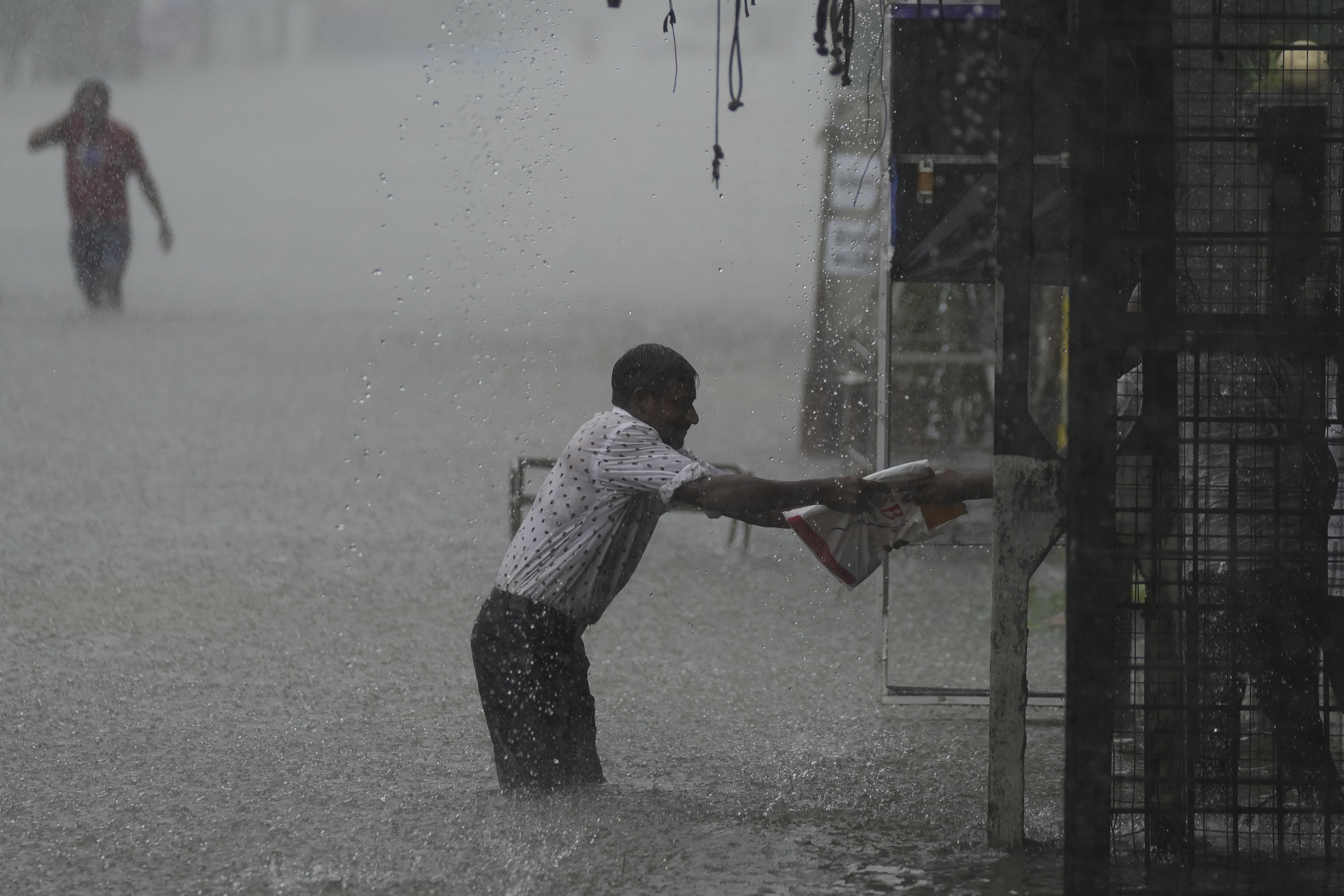 A man reaches for a safe place as it rains in a flooded street in Colombo, Sri Lanka, Sunday, Oct. 13, 2024. (AP Photo/Eranga Jayawardena)