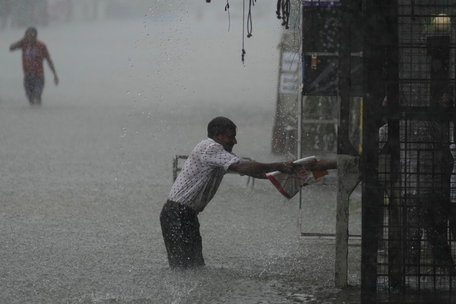 A man reaches for a safe place as it rains in a flooded street in Colombo, Sri Lanka, Sunday, Oct. 13, 2024. (AP Photo/Eranga Jayawardena)