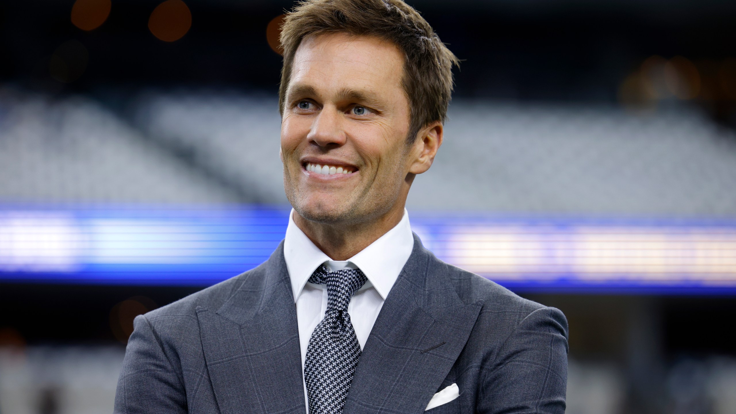 Fox Sports lead NFL analyst Tom Brady stands on the field during warmups before an NFL football game between the Detroit Lions and the Dallas Cowboys in Arlington, Texas, Sunday, Oct. 13, 2024. (AP Photo/Gareth Patterson)