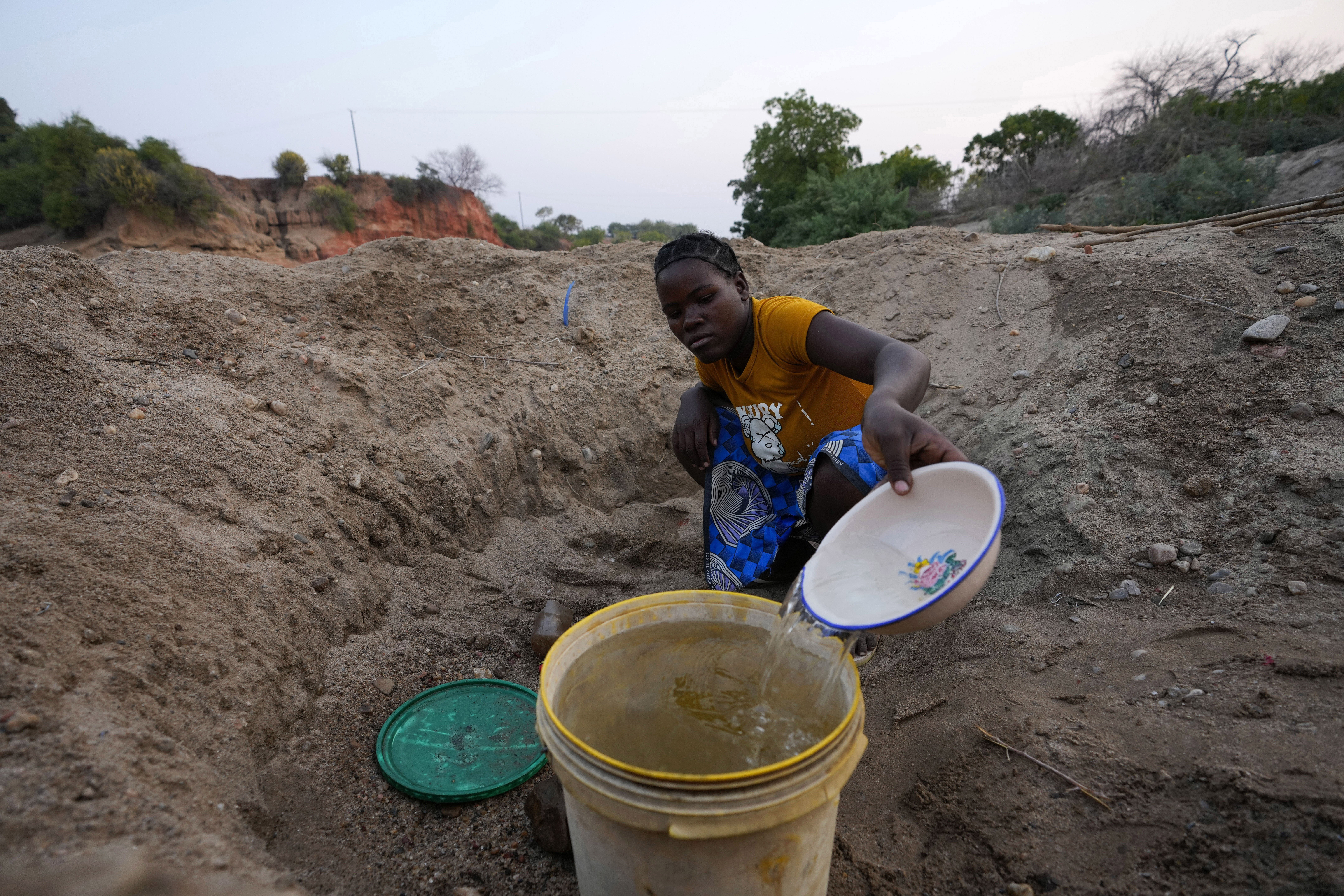 File — A woman scoops water from a hole she has dug in a dried up riverbed in Lusitu, Zambia, Wednesday, Sept. 18, 2024. (AP Photo/Themba Hadebe/File)