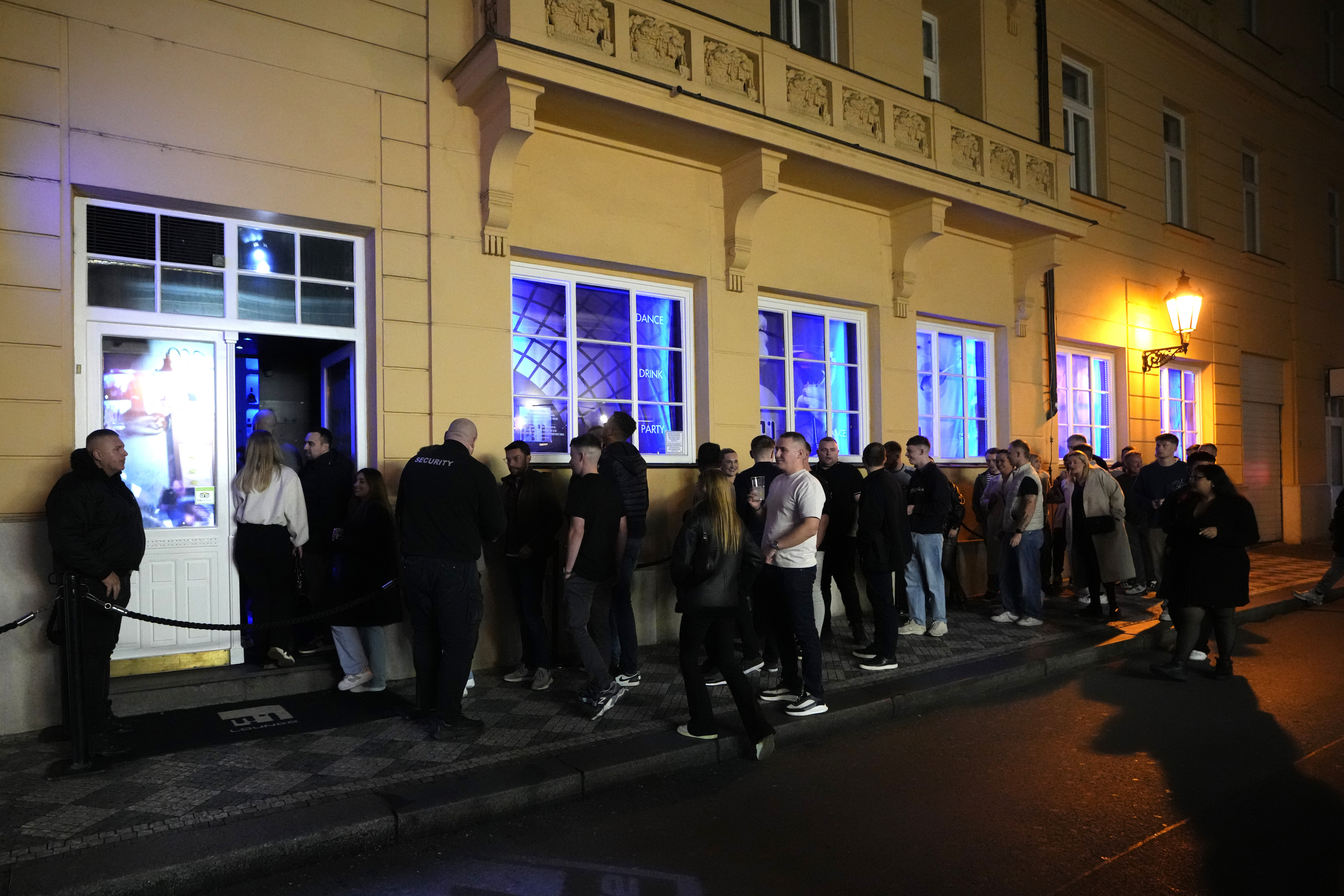 A group of tourists stand in line outside a bar as they attend a pub crawl tour in downtown Prague, Czech Republic, Thursday, Oct. 17, 2024. (AP Photo/Petr David Josek)