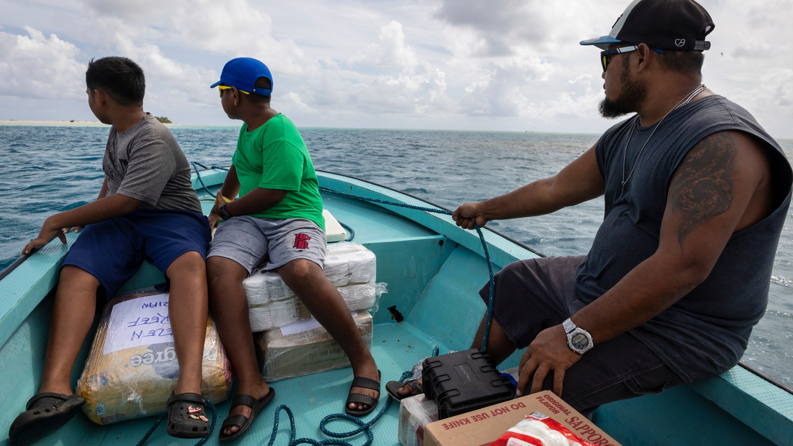 Metfidza Marino, from left, Aarson Aaron and Aaron Cyrillo look out to Helen Island, Palau, as a small speed boat transports toilet paper, dog food and other goods to the remote atoll on July 17, 2024. (AP Photo/Yannick Peterhans)