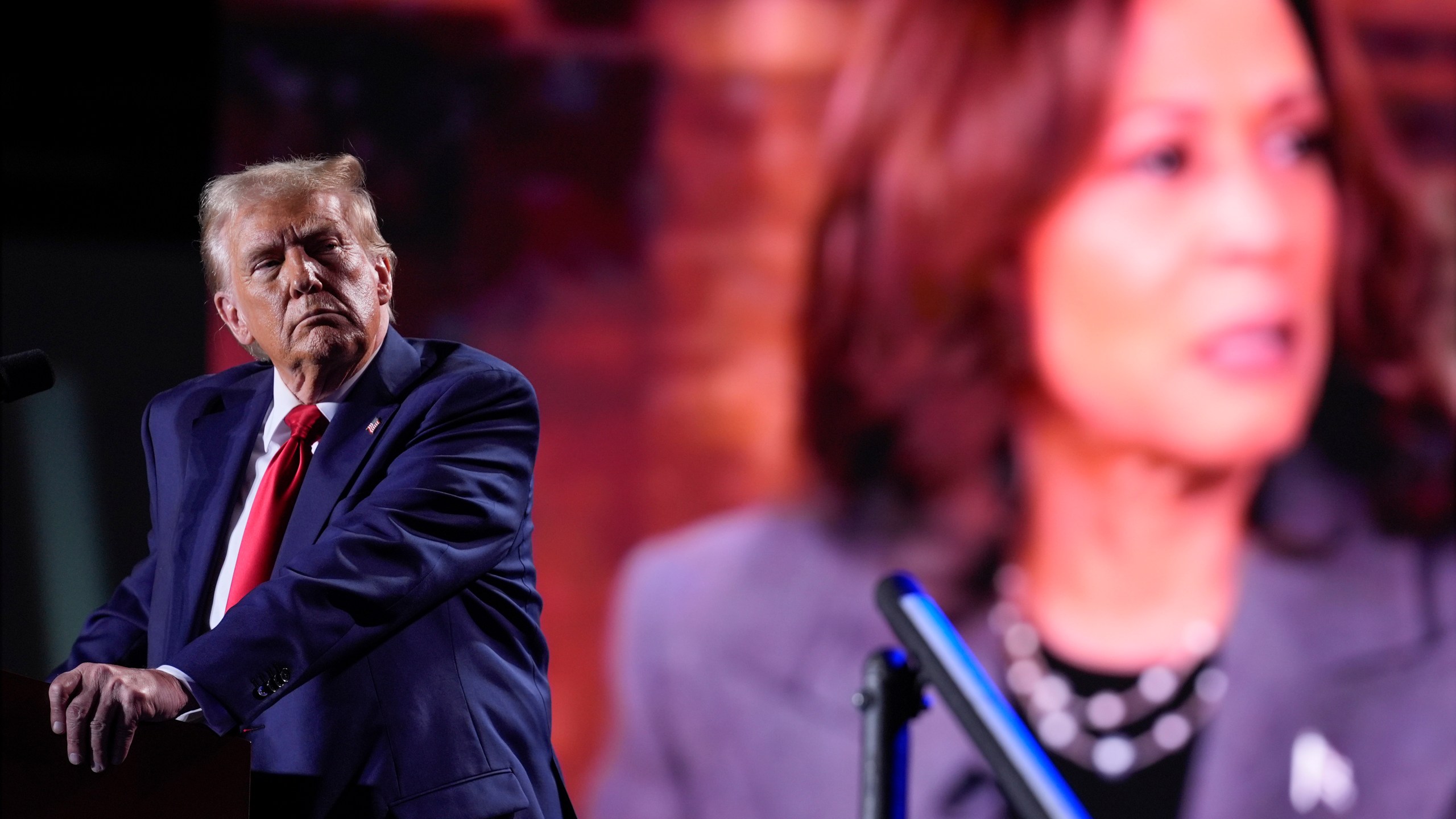 Republican presidential nominee former President Donald Trump watches a video on a screen with Democratic presidential nominee Vice President Kamala Harris as he speaks during a campaign event, Friday, Oct. 18, 2024 in Detroit. (AP Photo/Evan Vucci)