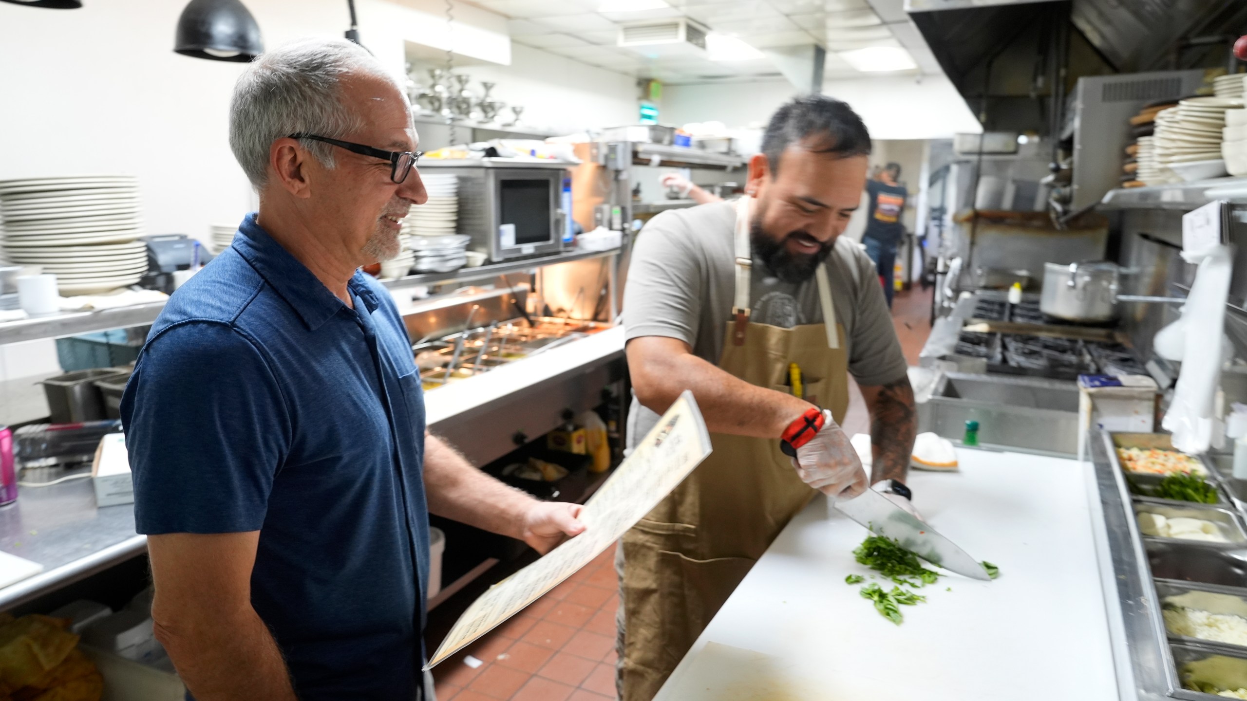 Dan Piacquadio, left, owner of Harold's Cave Creek Corral, waits to talk with chef and kitchen manager Lucio Osorno as he works in the kitchen as Piacquadio waits for the upcoming election and the results of Arizona Prop 138 on minimum wage Thursday, Oct. 3, 2024, in Cave Creek, Ariz. (AP Photo/Ross D. Franklin)