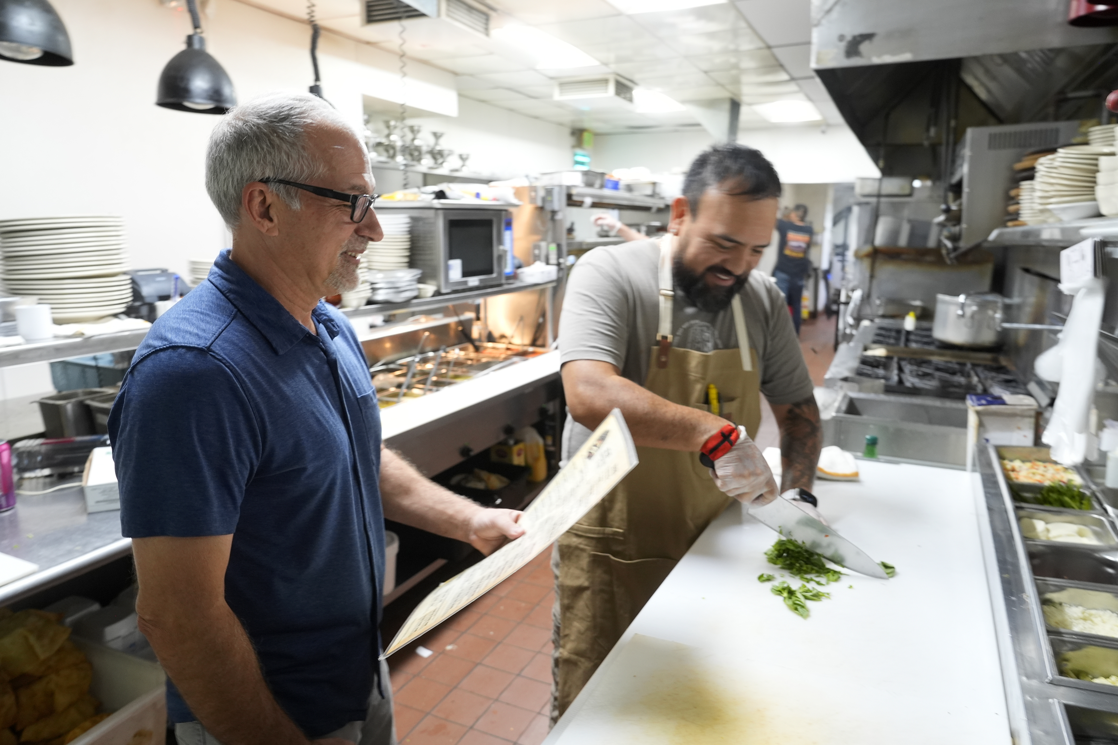 Dan Piacquadio, left, owner of Harold's Cave Creek Corral, waits to talk with chef and kitchen manager Lucio Osorno as he works in the kitchen as Piacquadio waits for the upcoming election and the results of Arizona Prop 138 on minimum wage Thursday, Oct. 3, 2024, in Cave Creek, Ariz. (AP Photo/Ross D. Franklin)