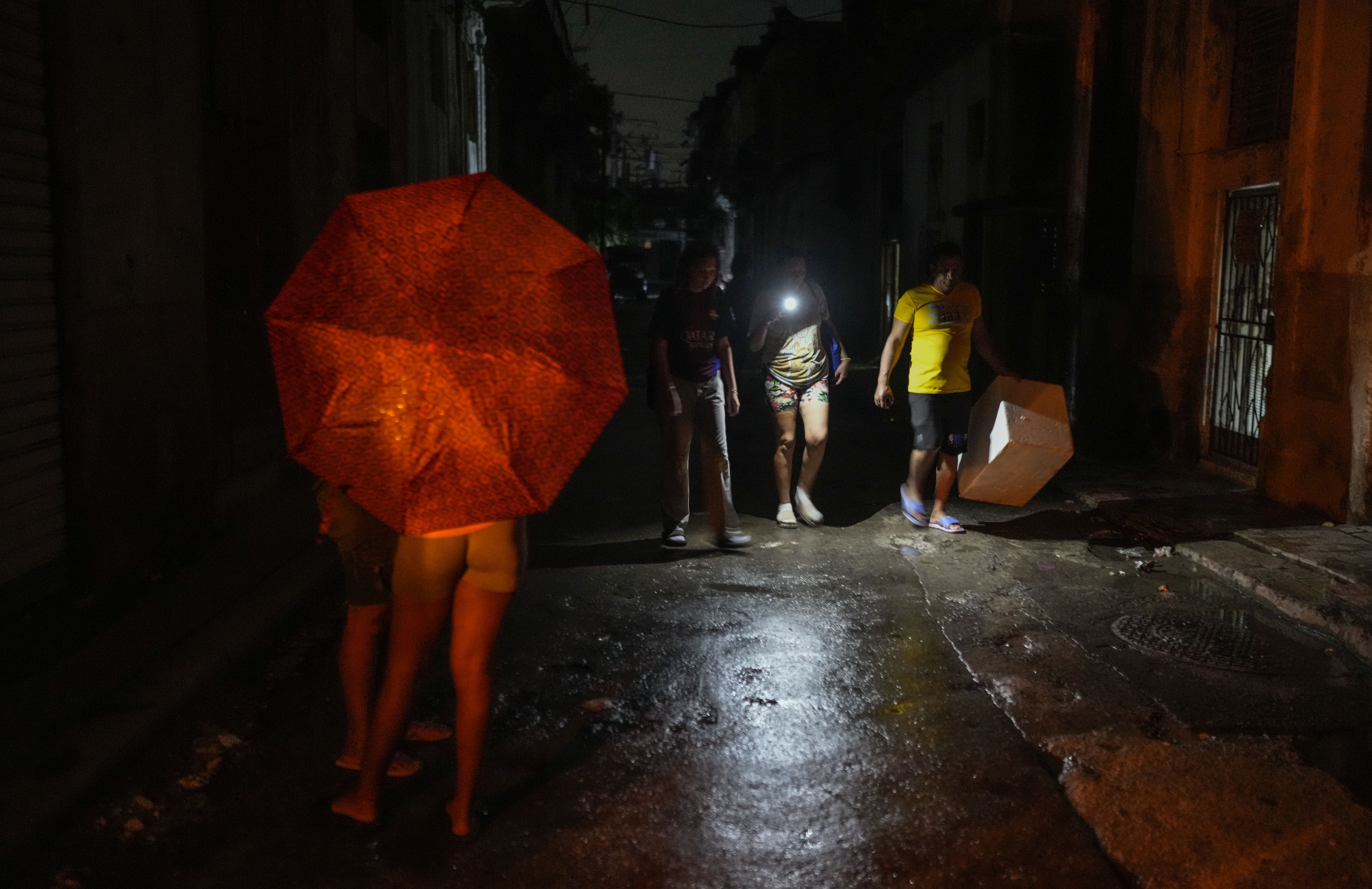 Residents walk down a street using a phone flashlight during a power outage following the failure of a major power plant in Havana, Cuba, Saturday, Oct. 19, 2024. (AP Photo/Ramon Espinosa)